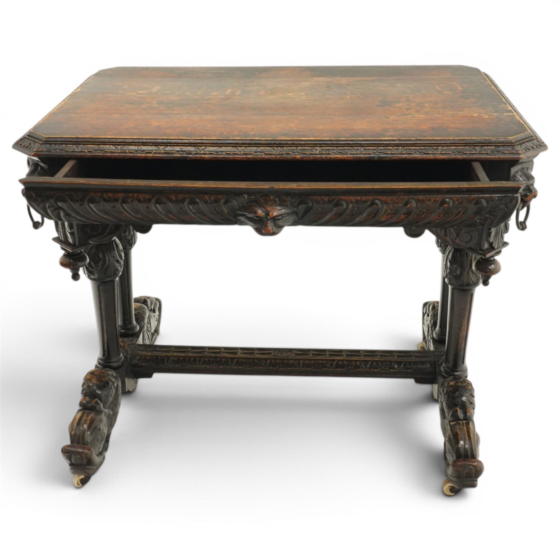 Victorian Jacobean Revival heavily carved oak centre table , rectangular top with canted corners and carved edge, fitted with single frieze drawer with central carved green-man handle with flanking gadrooning, the corners with lion masks, raised on fluted supports terminating to splayed stylised dolphin feet with castors, united by stretcher