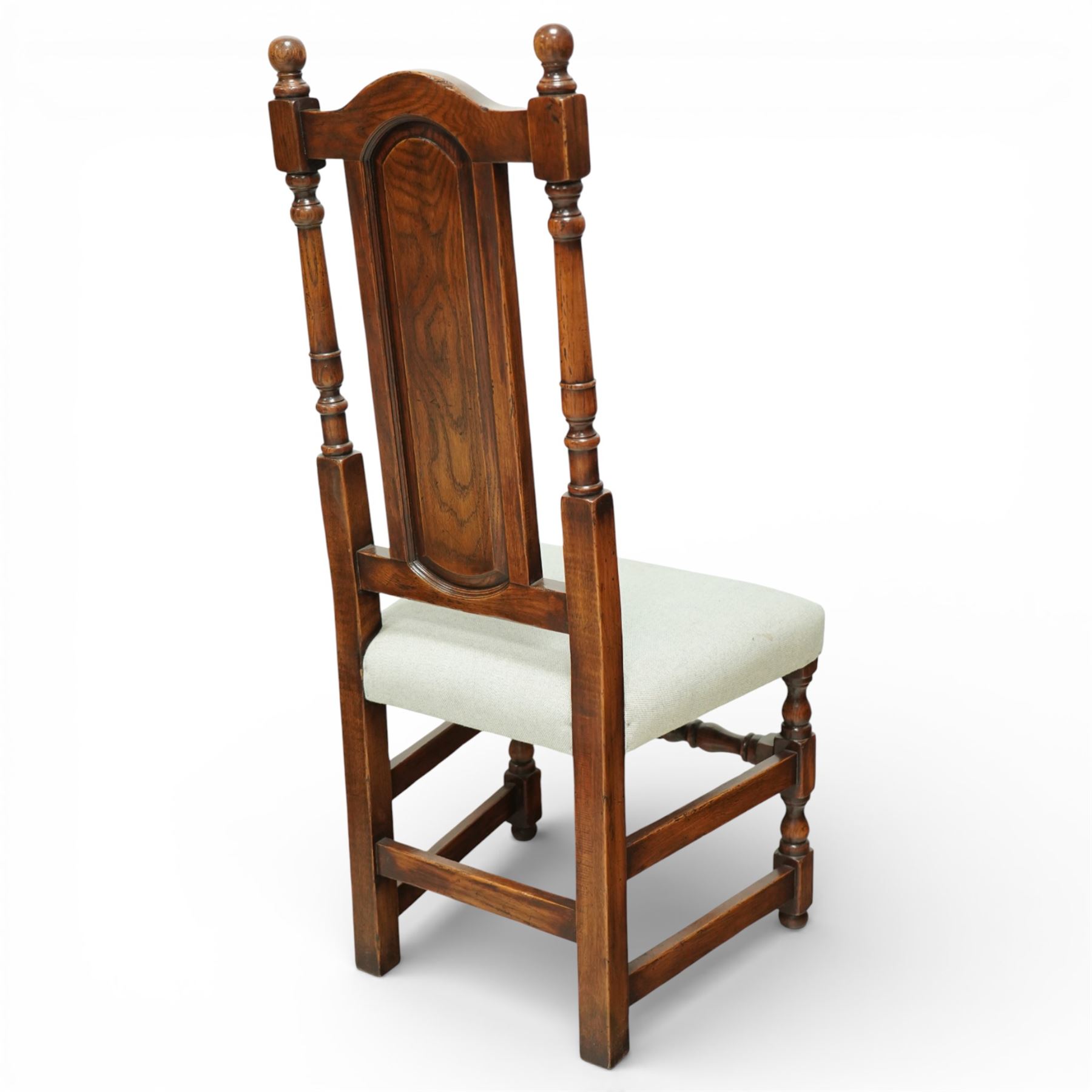 Country House oak high back dining chairs, set of ten comprising eight side chairs and two carvers, each with arched top rail flanked by turned finials over a central fielded panel back, with overstuffed seats upholstered in pale fabric, raised on turned front supports united by stretchers