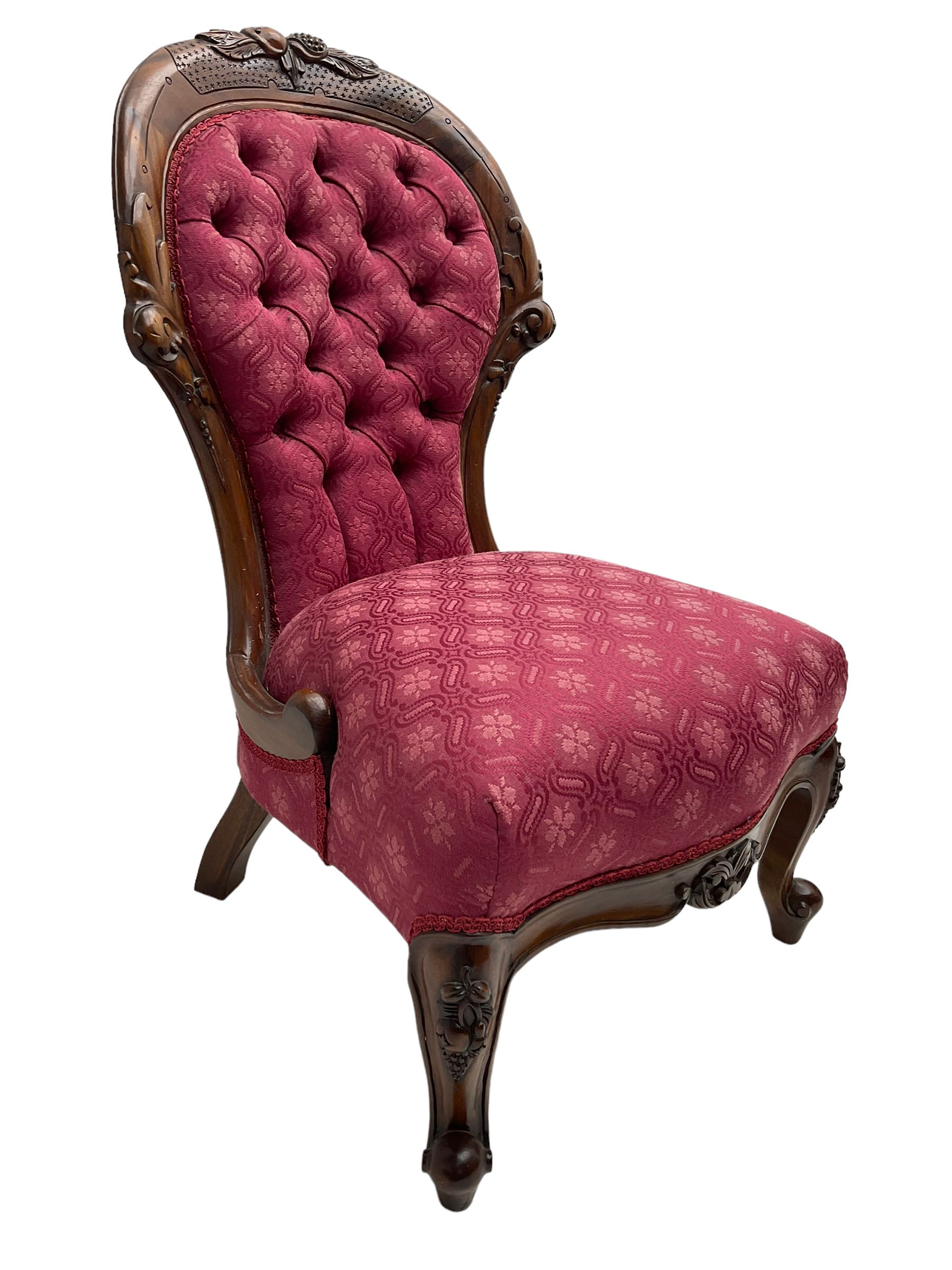 Victorian style mahogany framed nursing chair, the cresting rail carved with fruit and foliage, upholstered in red patterned fabric with buttoned back, on cabriole supports with scrolled terminals