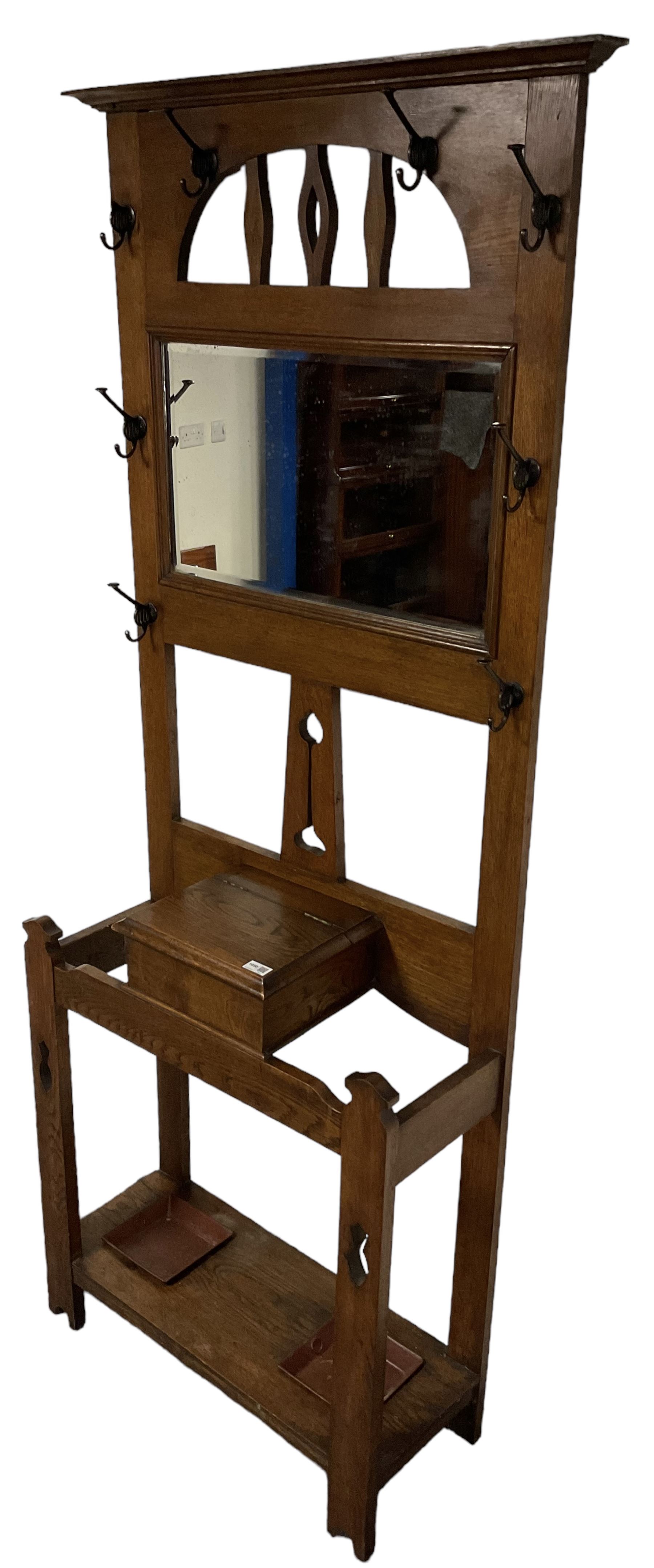 Arts & Crafts period oak hall stand, projecting moulded cornice over arched cut-out decorated with shaped vertical rails, fitted with rectangular bevelled mirror back over hinged glove compartment, on straight pierced supports with shaped pediments 