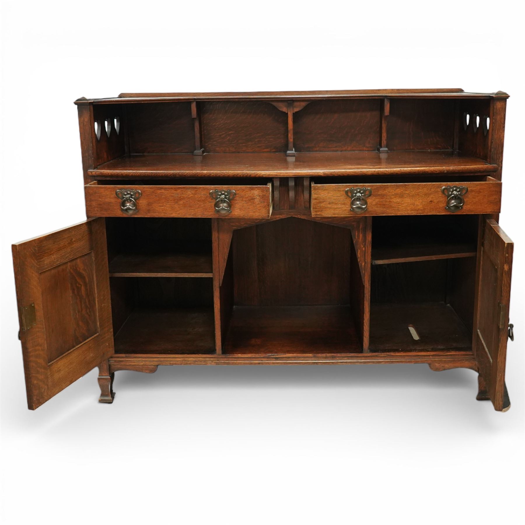 Shapland and Petter - Arts and crafts oak sideboard, rectangular overhanging top with raised open back fitted with shaped supports and pierced heart cut-outs to the ends, the base fitted with a central arrangement of two short drawers with cast metal drop handles over an open kneehole recess, flanked by a pair of cupboard doors each with linenfold panels and applied strap hinges, enclosing shelved interiors, raised on shaped bracket feet