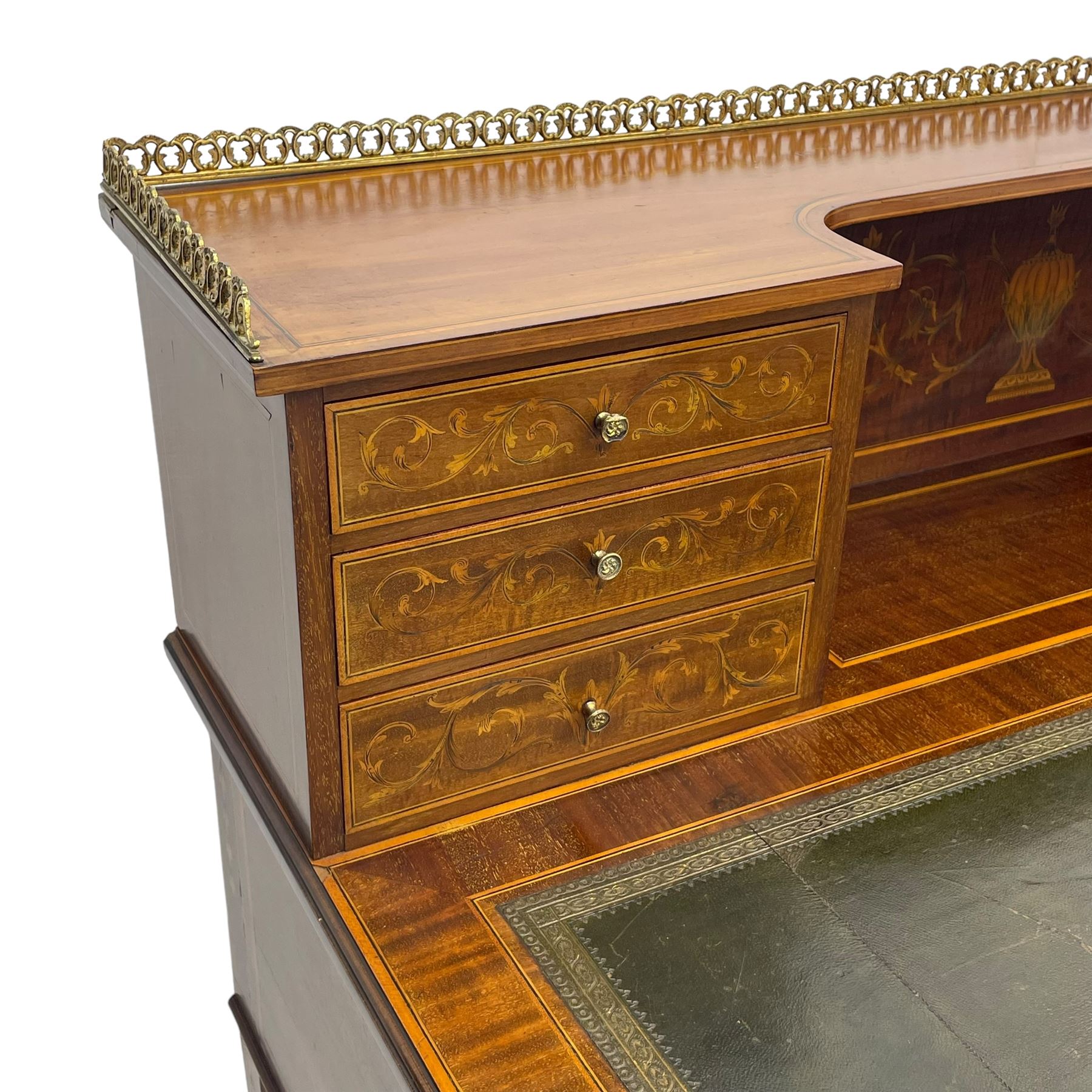 Edwardian inlaid mahogany writing desk, raised galleried back over inlaid central urn with scrolling leafy branches and six small drawers, satinwood banded rectangular moulded top with tooled leather inset, fitted with five drawers, the drawer facias inlaid with scrolling foliage and satinwood banding, square tapering supports inlaid with trailing bell flowers, on brass and ceramic castors 