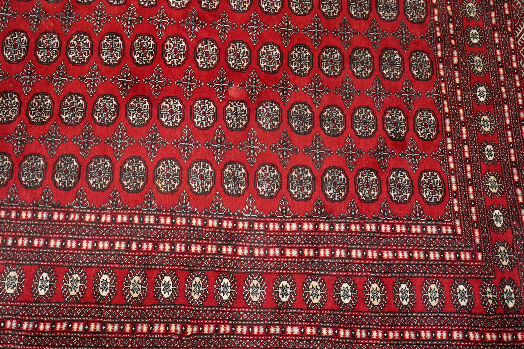 Large crimson ground Afghan Bokhara carpet, the field decorated with repeating Gul and geometric motifs, the multiple guard stripes with further geometric decoration