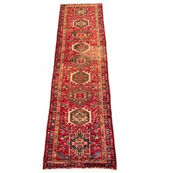 Persian Karajeh red ground runner, the field set with nine trailing geometric medallions, decorated all over with stylised motifs, geometric design with multiple banded border