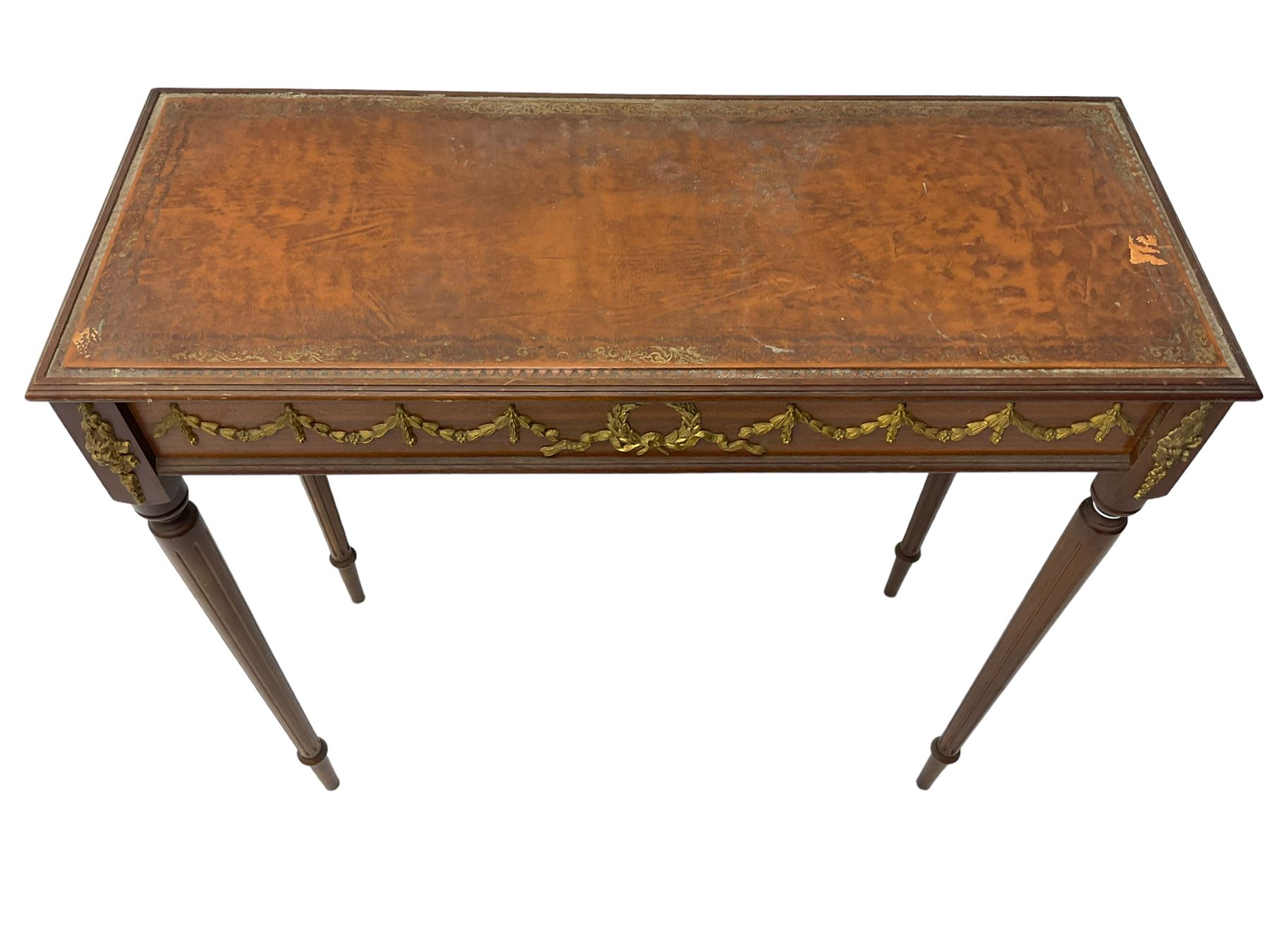 Early 20th century mahogany side table, inset amber leather surface, frieze decorated with applied gilt festoons and central wreath, on tapering fluted supports