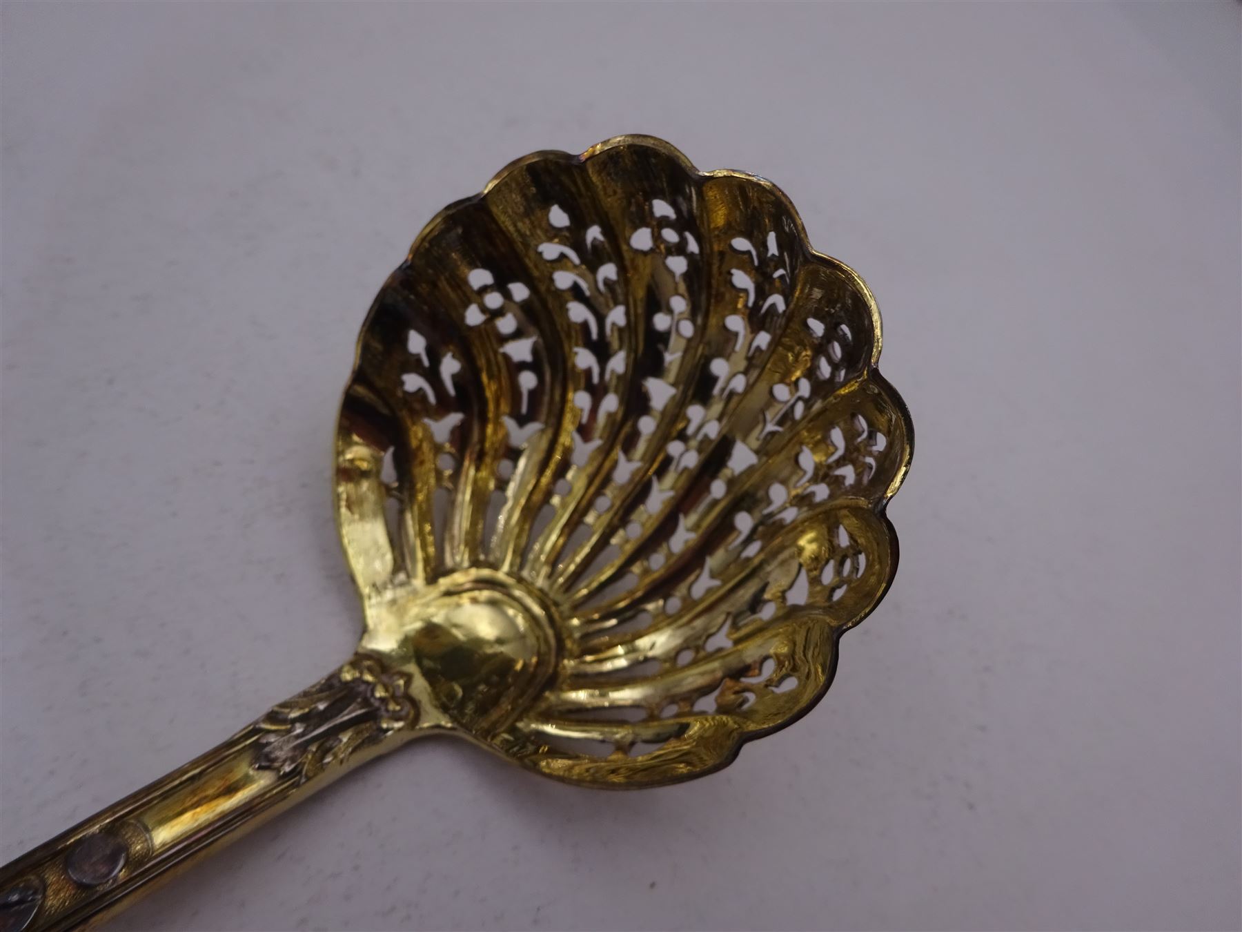 Victorian silver-gilt sugar sifting spoon, with gilded pierced shell shaped bowl, the handle decorated in relief with classical greek figures amongst fruiting vines, hallmarked Henry John Lias & James Wakely, London 1874,  L16cm, contained within tooled leather silk and velvet lined fitted case