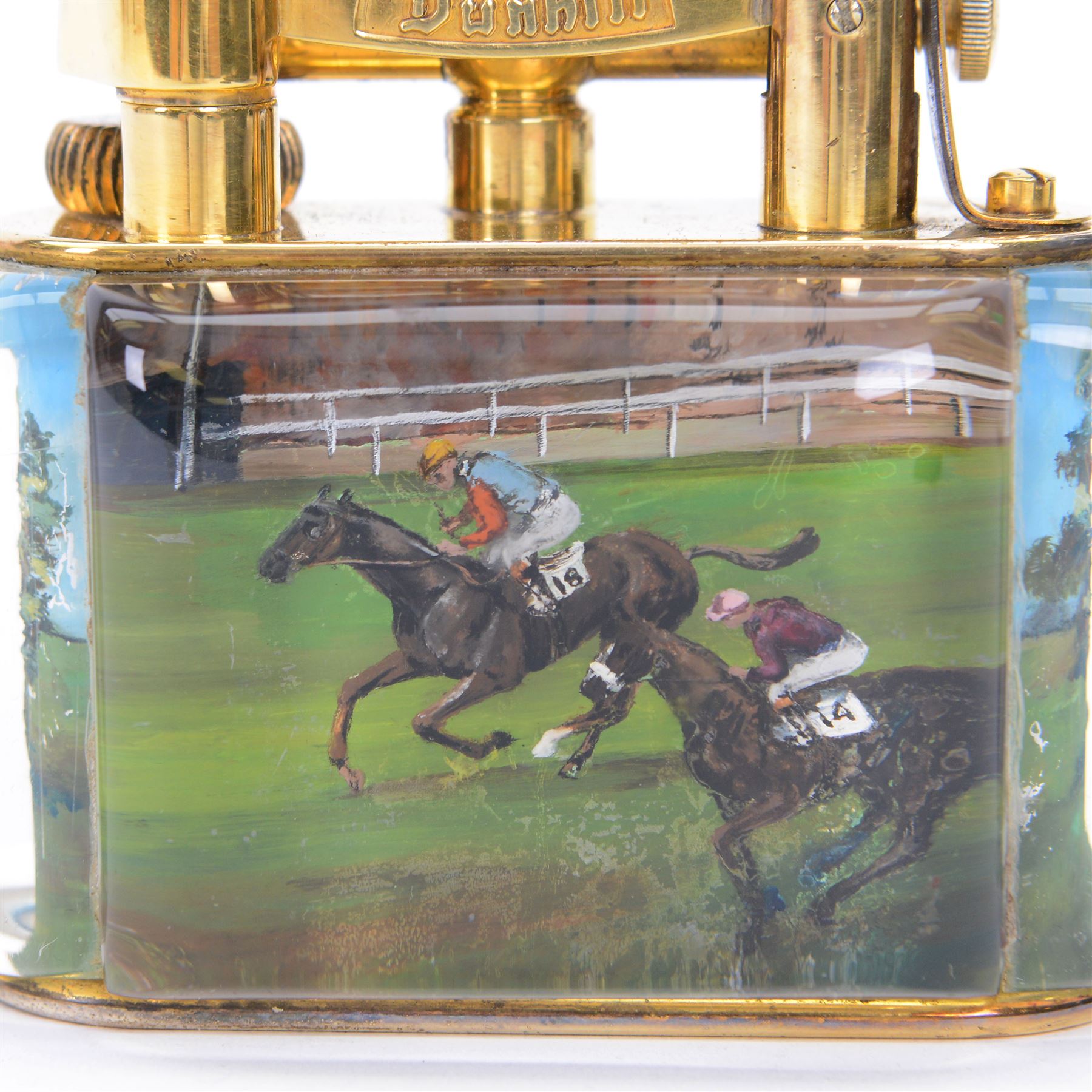 Rare one off special commission Dunhill Sporting Horse Racing half-giant 'Aquarium' table lighter, circa 1955, the lucite panelled body engraved in reverse intaglio technique and hand-painted with Nicholas Nickleby in action, winner of the Royal Hunt Cup, Ascot June 1955, the reverse with jockey Willie Snaith mounted upon Nicholas Nickleby, the gold plated top with arm stamped Dunhill Reg. No 737418, the base stamped DUNHILL LIGHTER, H7.5cm W10cm D5cm

Provenance:
Commissioned by the owner of Nicholas Nickleby, the lighter was gifted to Colin Hetherton, a young veterinary surgeon whose intervention saved Nickleby from certain retirement. Hetherton’s expert care and persistence brought the horse back to full health, culminating in a win that stunned the Ascot crowd.