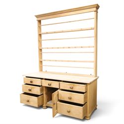 Victorian stripped pine dresser base with plate rack, the four-tier plate rack with supporting rails and hooks, the inverted-breakfront base fitted with seven assorted graduating drawers surrounding a recessed cupboard, on compressed bun feet with castors