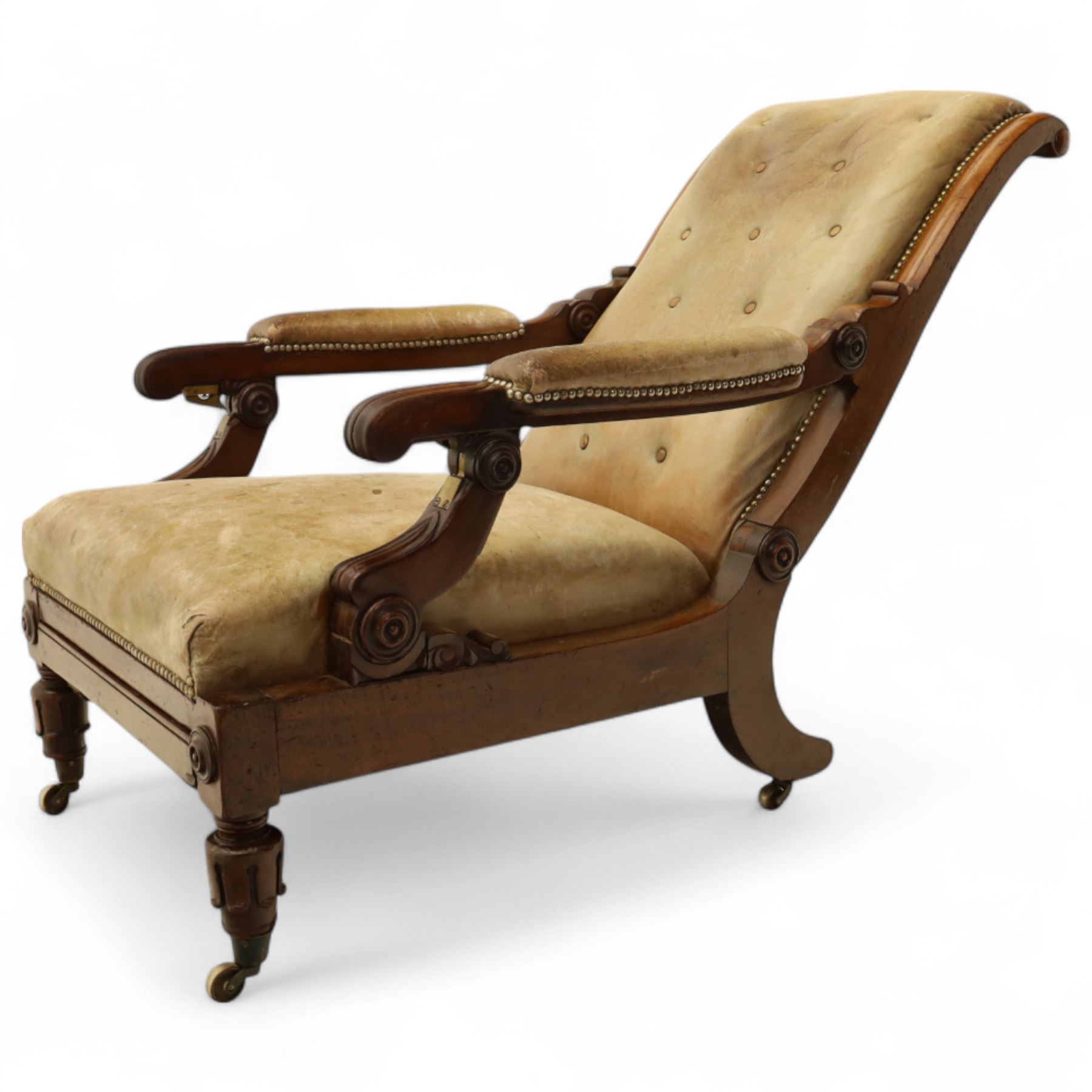 William IV mahogany gentleman's library reclining armchair, leather button upholstered and brass-studded back and seat, above leather-covered arms terminating with carved roundels and foliate scroll-carved ends, underside with brass mechanical trigger reclining lever, the apron with retractable foot rest, supported on lappet carved and turned legs with brass castors, circa 1835