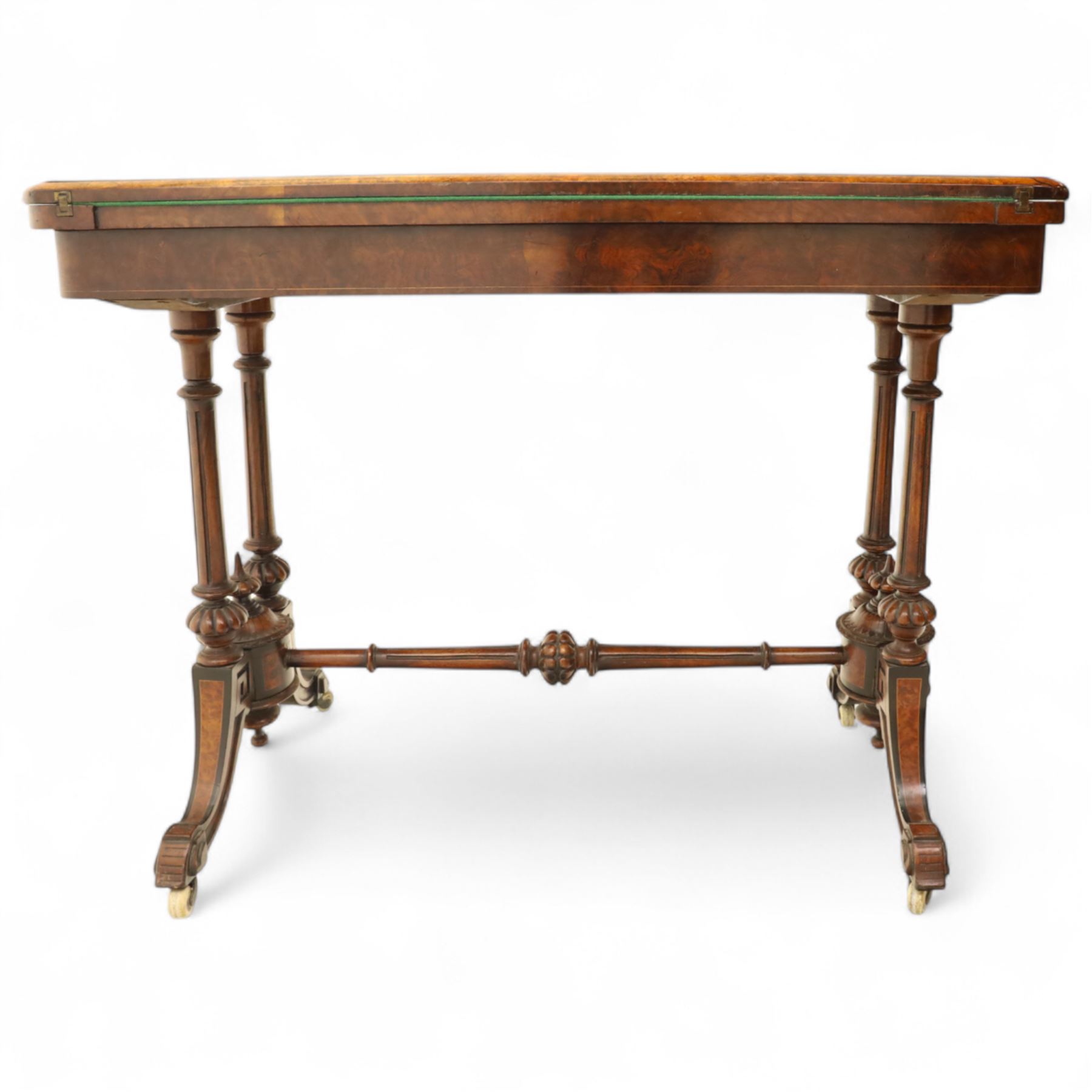 Victorian walnut and inlaid games table, rectangular fold-over top with figured walnut veneers and foliate inlay, swivel and fold over to reveal a green baize lined playing surface, on twin supports united by a stretcher, raised on scroll carved feet with castors (extended 96cm x 92cm)