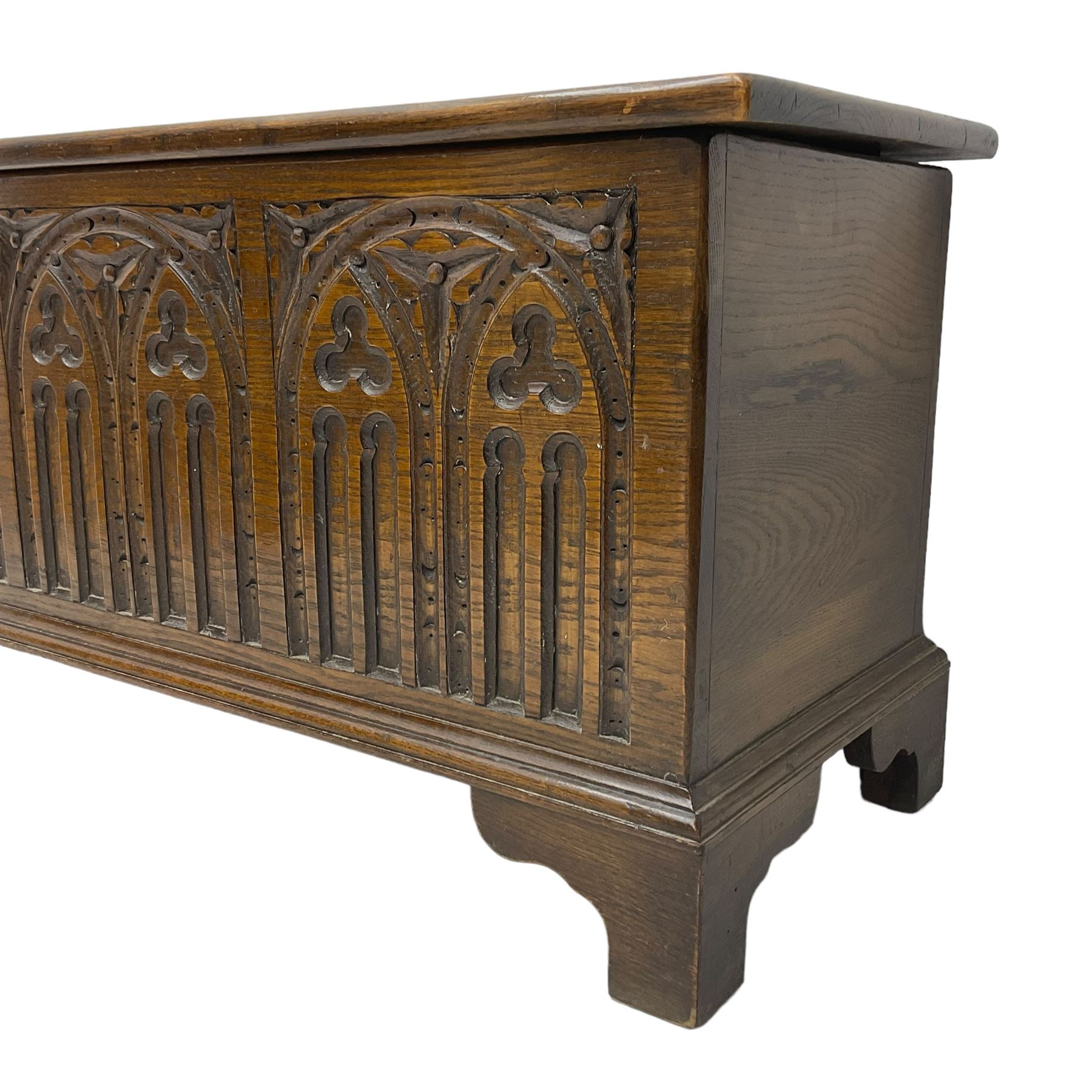 Mid-20th century oak blanket box, hinged lid over front carved with Gothic tracery work and flower heads, on bracket feet