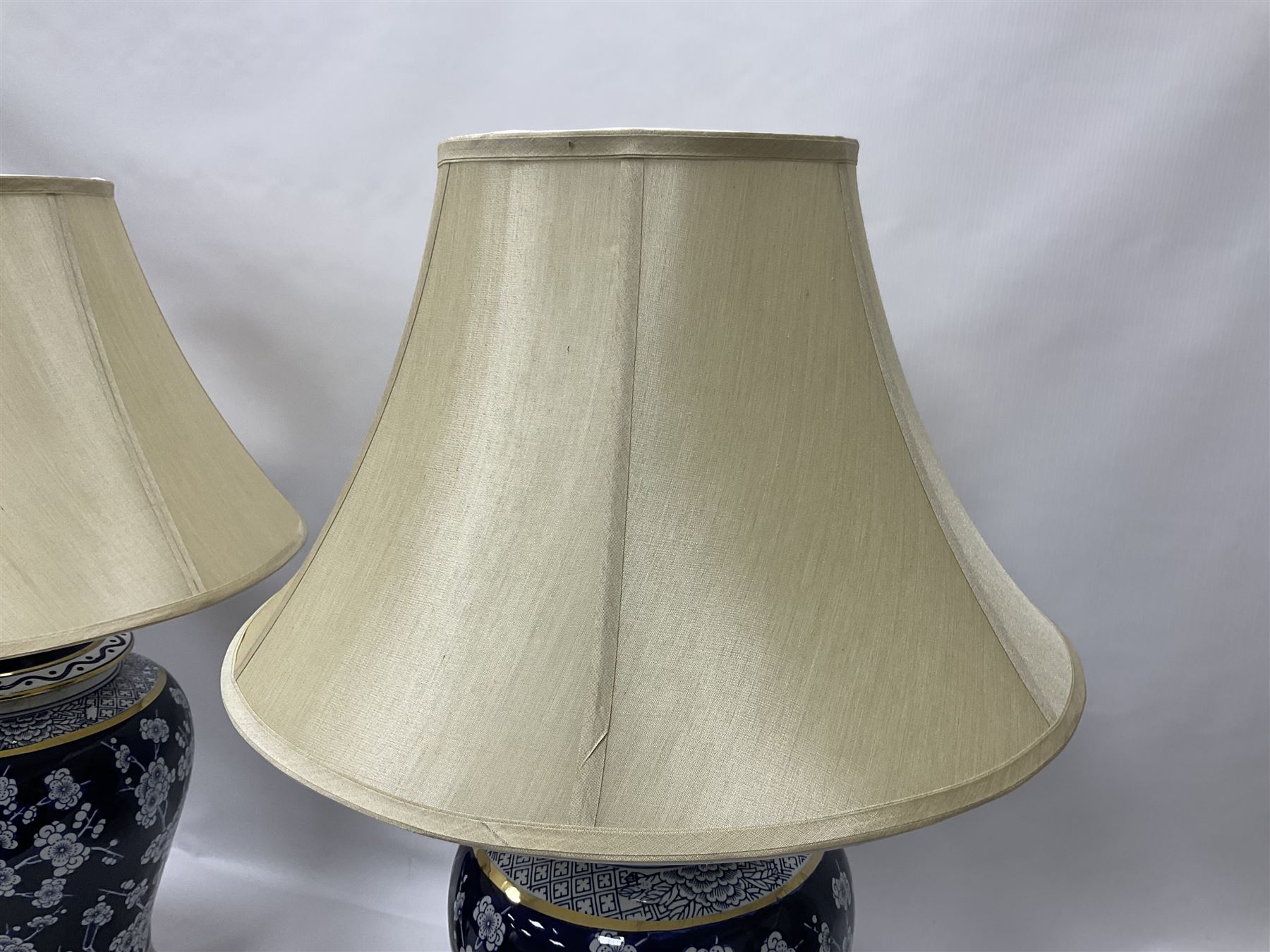 Pair of blue and white table lamps, each of baluster form, decorated with prunus blossom, within stylised borders, raised upon circular gilt base, excluding fittings H48cm