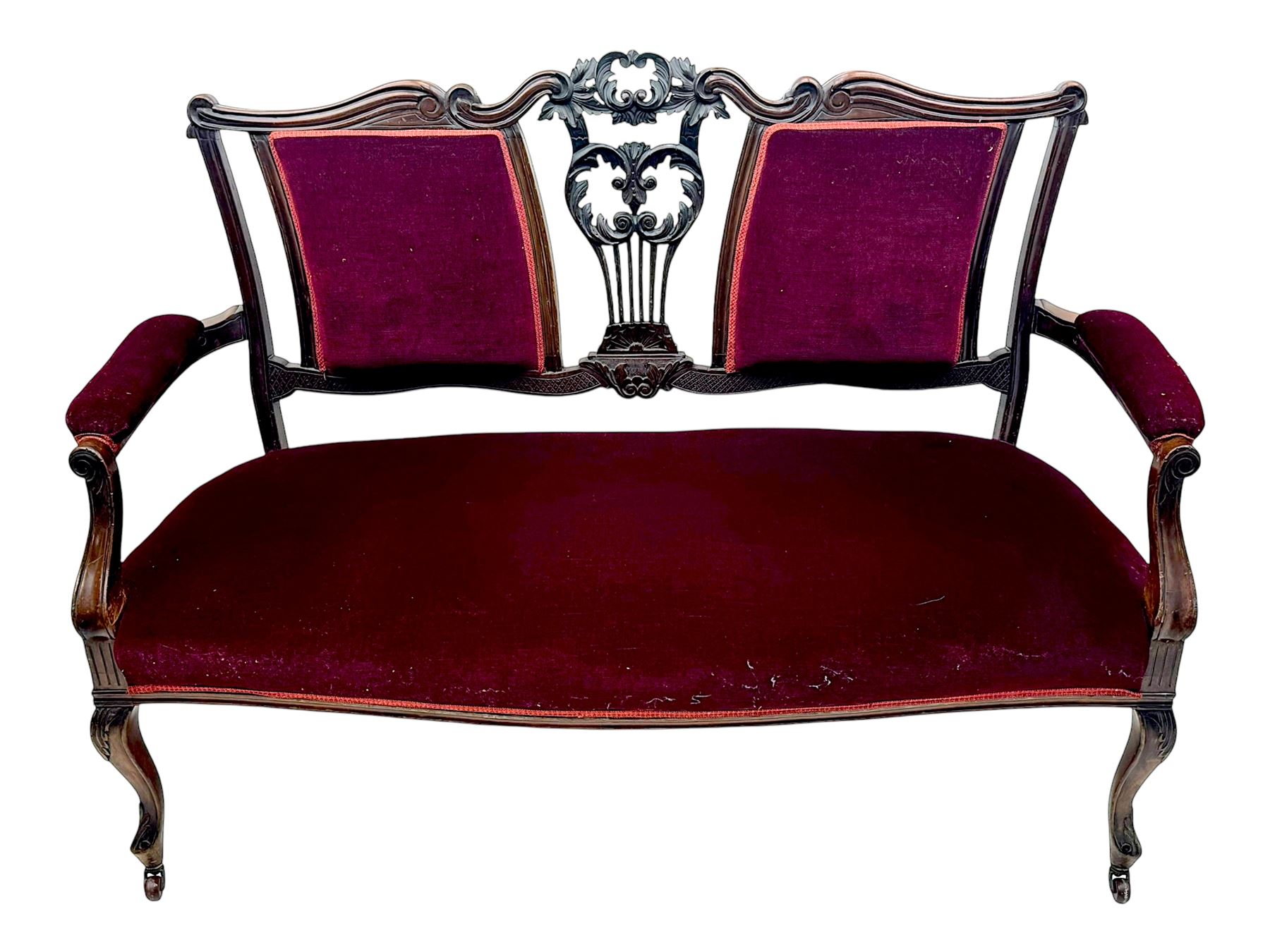 Late Victorian stained beech framed sofa, the backrests, seat and padded arms upholstered in deep red fabric, carved crest rail with scroll and foliate motifs supported by carved uprights, on cabriole supports with leaf carvings terminating in castors