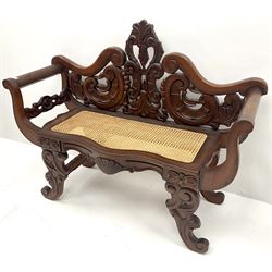 Hardwood two seat bench, floral carved and pierced back, scrolling arms, cane seat