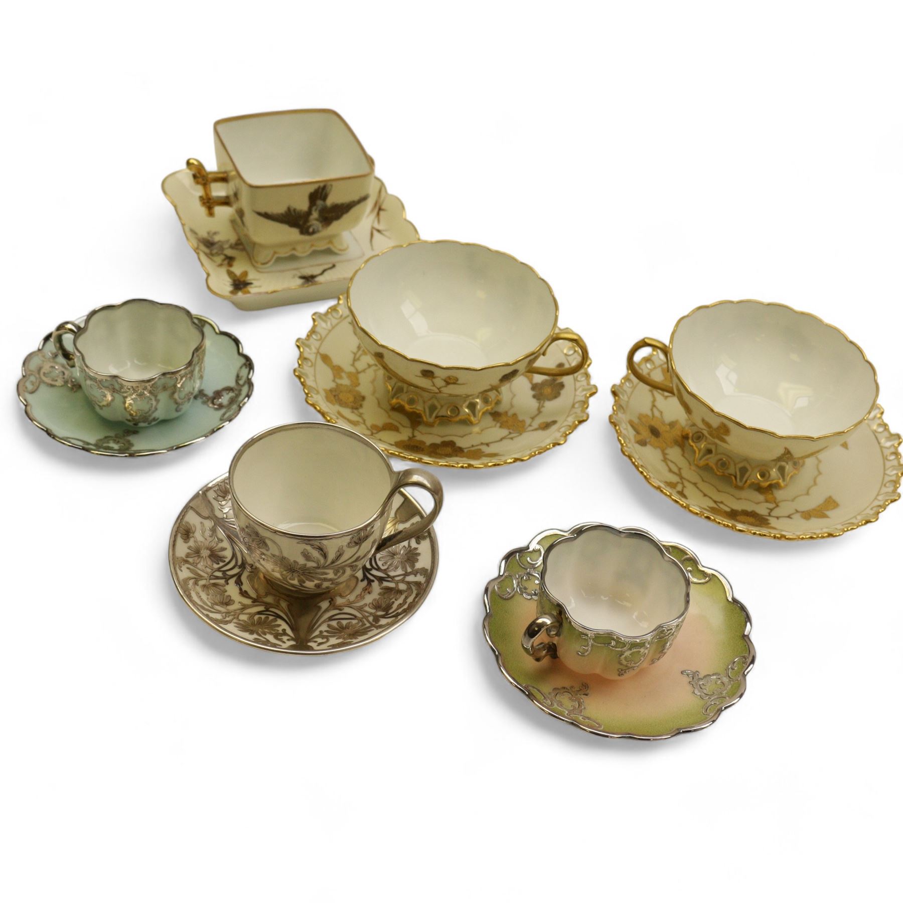 Three Pirkenhammer cups and saucers, two decorated with gilt birds in foliage on an ivory ground, the other with butterflies and foliate sprigs together with three  continental cups and saucers decorated with silver overlay 