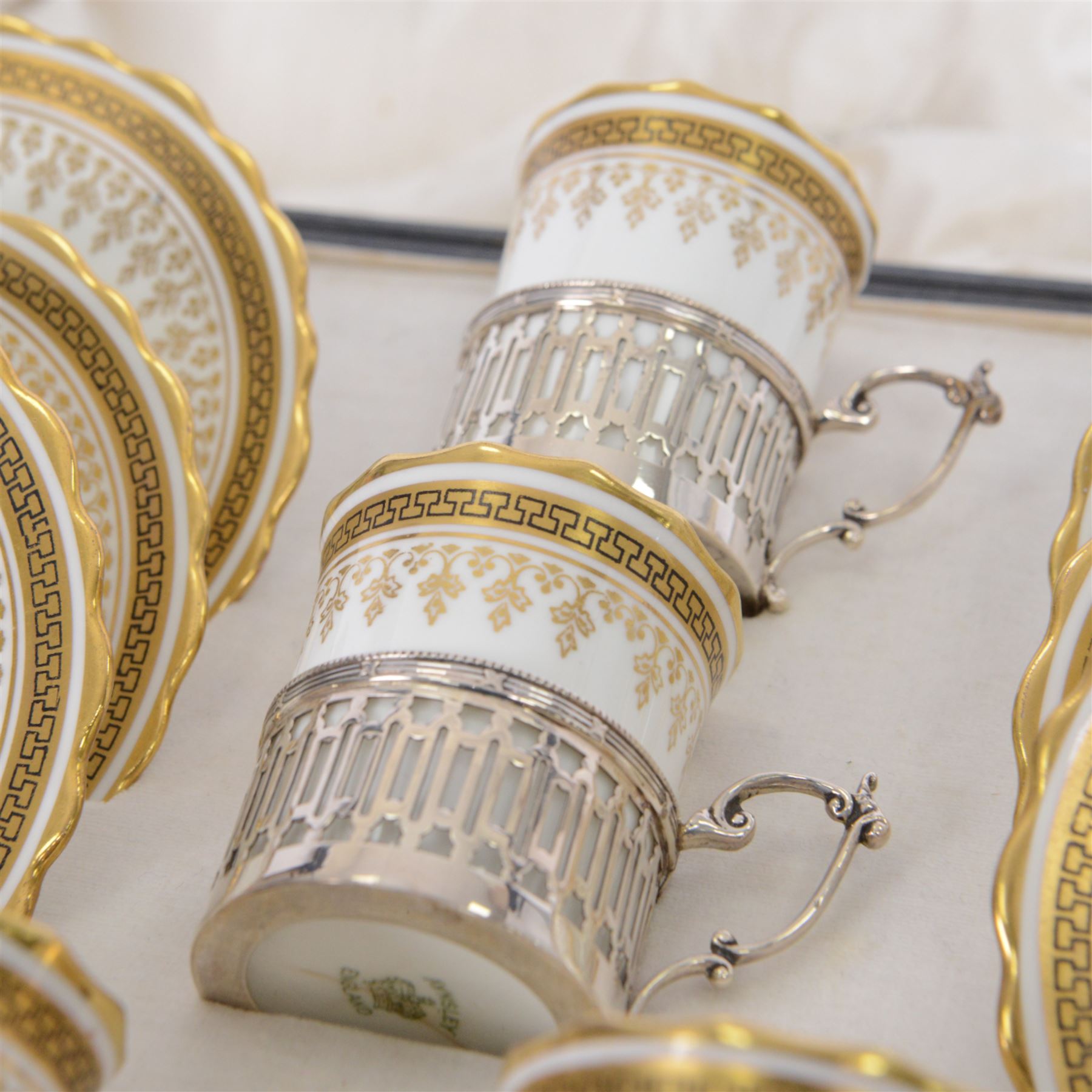 Boxed set of six Aynsley coffee cans and saucers, decorated with gilt greek key border, the cans within silver mounts, hallmarked Birmingham 1911