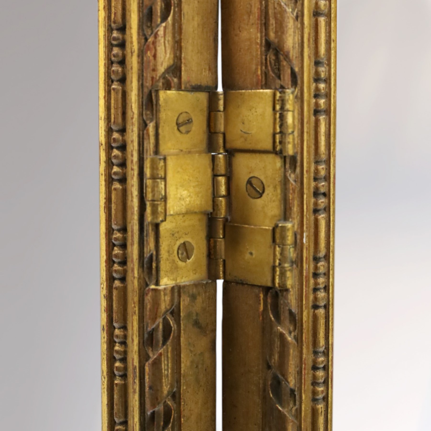 Early 20th century gilt and bevelled mirrored four panel folding screen, with two mirrors per side, flanked by beaded edges and scrolled finials, arcaded carved frieze