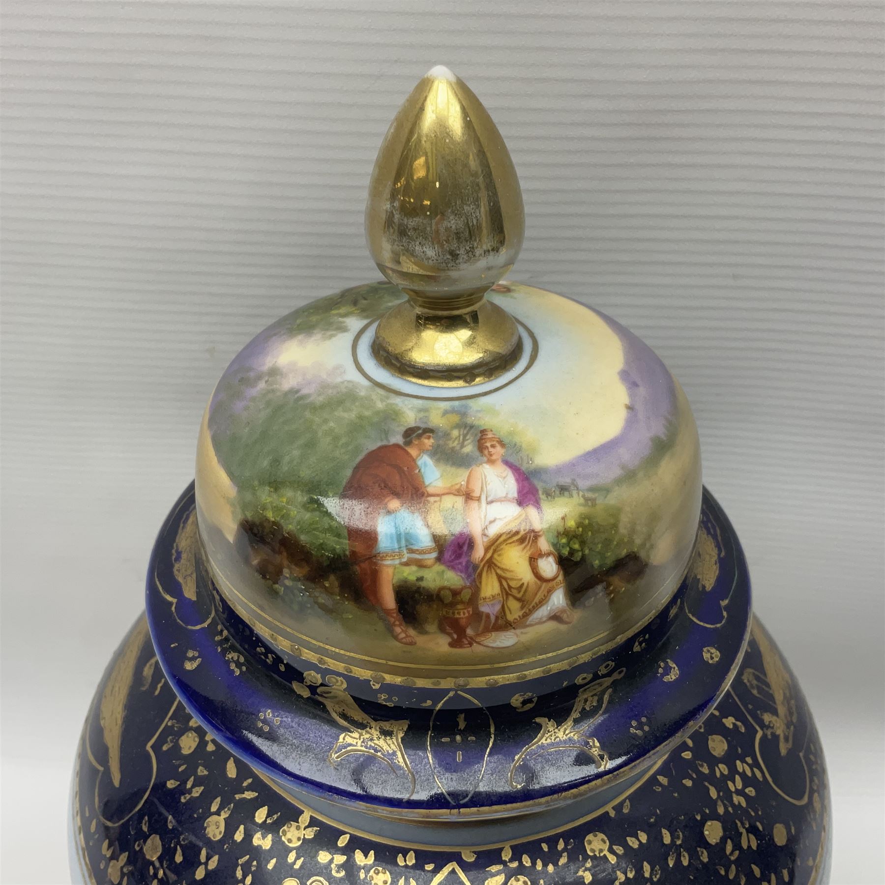 19th century Vienna style porcelain 'Musik' garniture, the central vase of baluster form with domed cover flanked by two smaller vases with twin curved gilt handles to short neck, each decorated with classical figural vignettes between blue borders heightened with gilt, H33.5cm