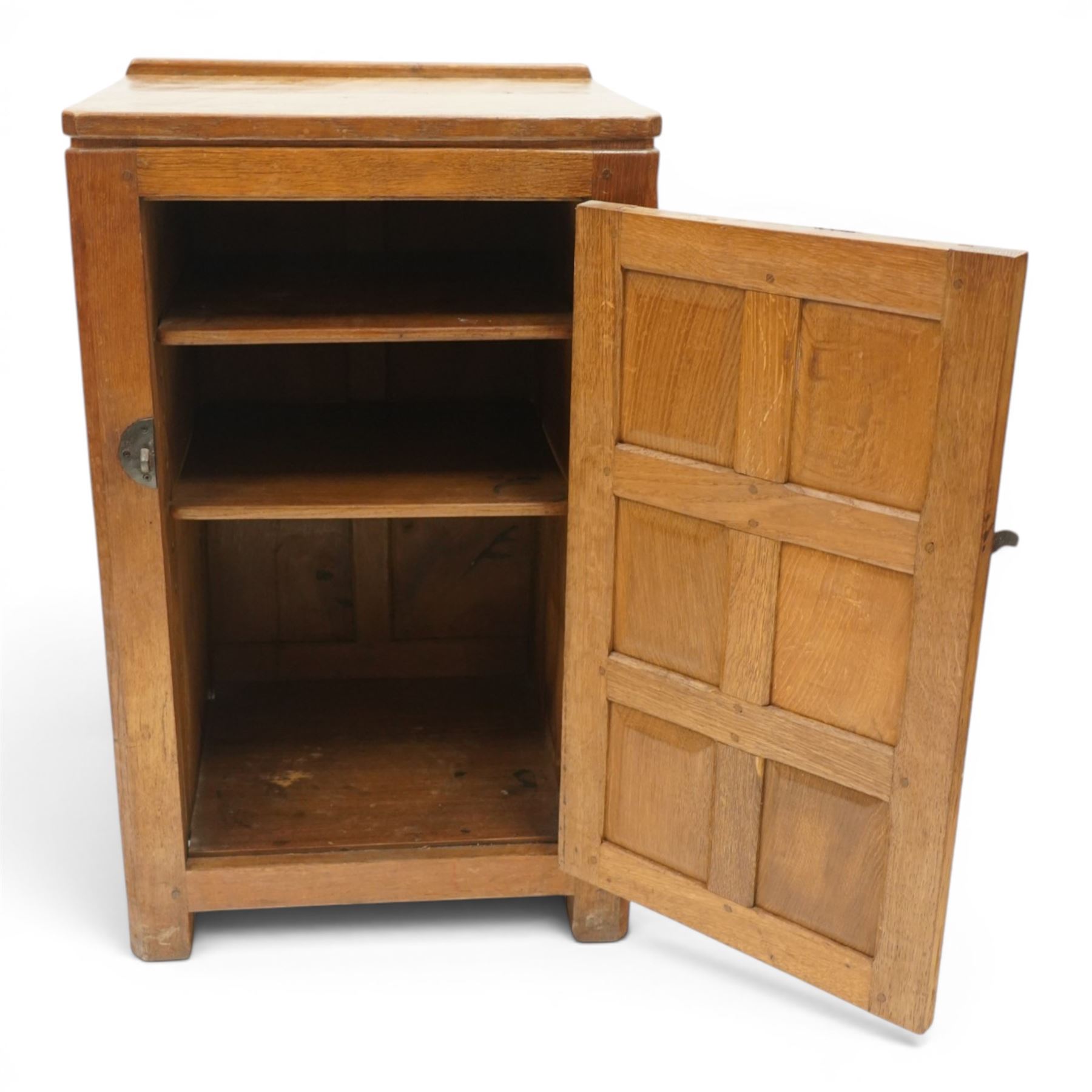 Mouseman - early-to-mid-20th century adzed and panelled dark oak bedside cupboard, raised back over rectangular canted top, fitted with single panelled cupboard door with chamfered rails and wrought iron fittings, enclosing two adjustable shelves, raised on canted square feet, carved with mouse signature, by the workshop of Robert Thompson of Kilburn
