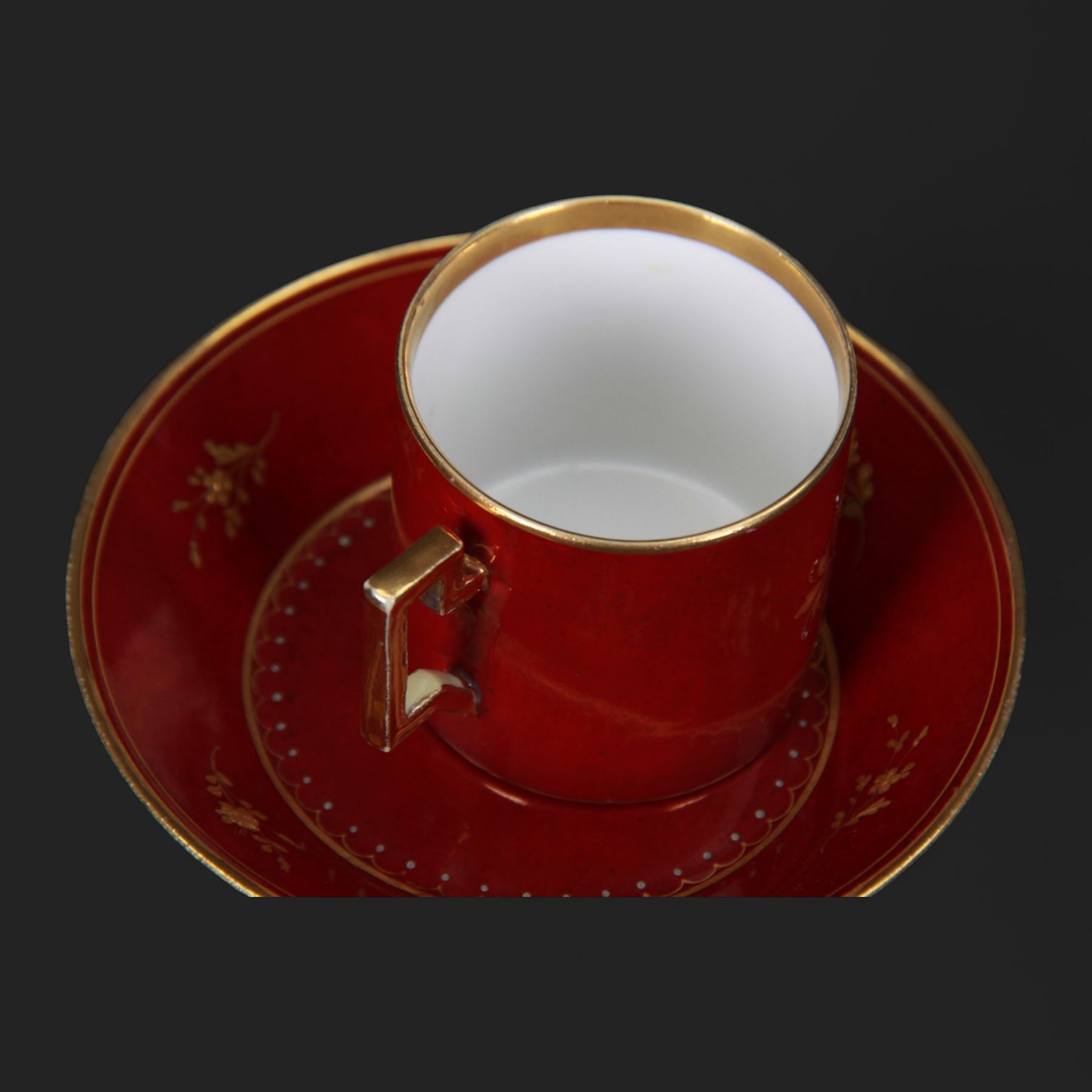 Late 19th century Vienna style coffee can and saucer, the cup with oval panel containing hand painted portrait of a gentleman, within a gilt foliate detailed surround, and upon a burgundy ground, the saucer with gilt band and sprigs upon a burgundy ground, with spurious shield mark beneath, cup H5cm saucer D12cm