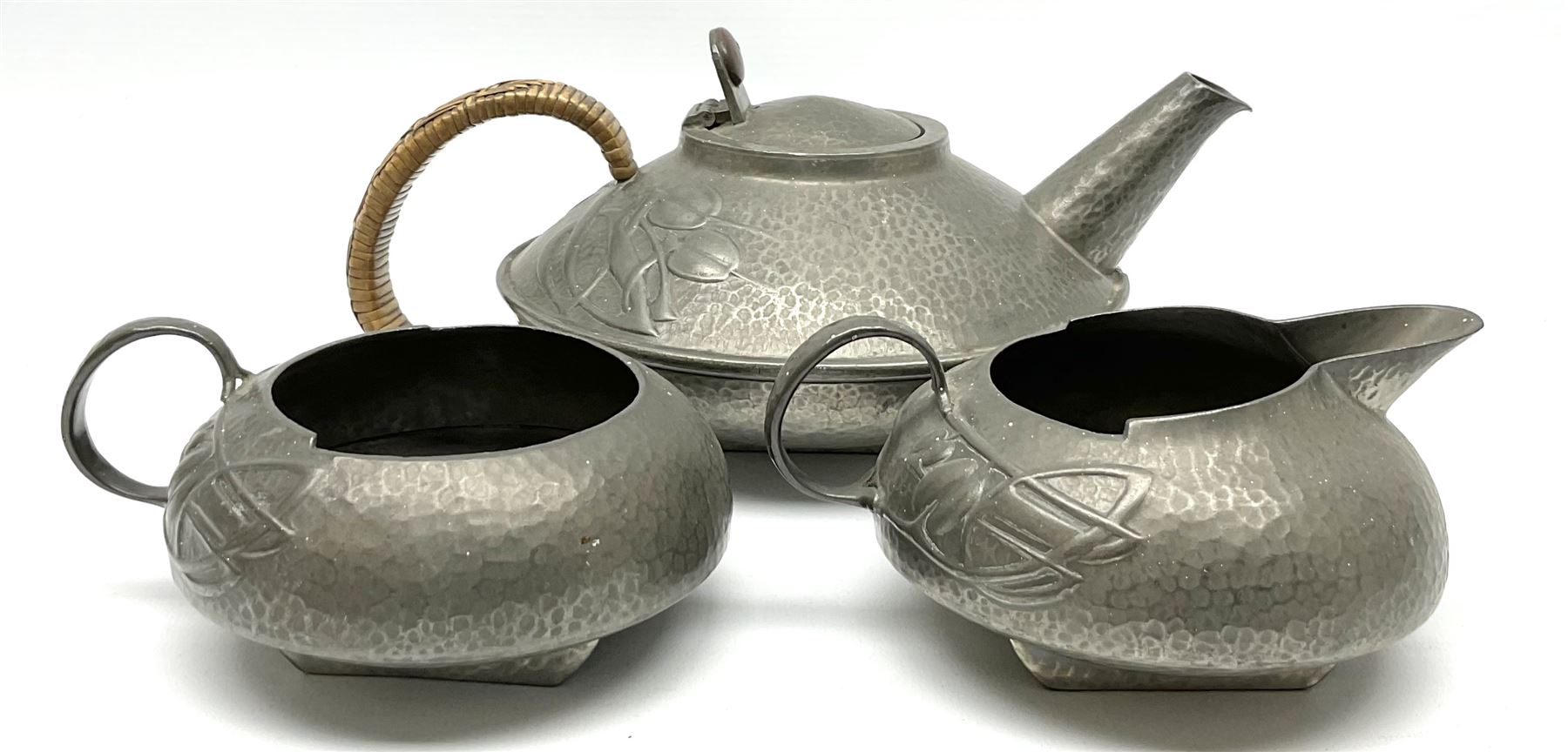 Archibald Knox for Liberty & Co Tudric pewter three piece tea service, comprising teapot with woven reed handle, single handled open sucrier, and milk jug, each with planished finish and detailed with honesty flowers, each impressed beneath Made in England Tudri Pewter 0231 