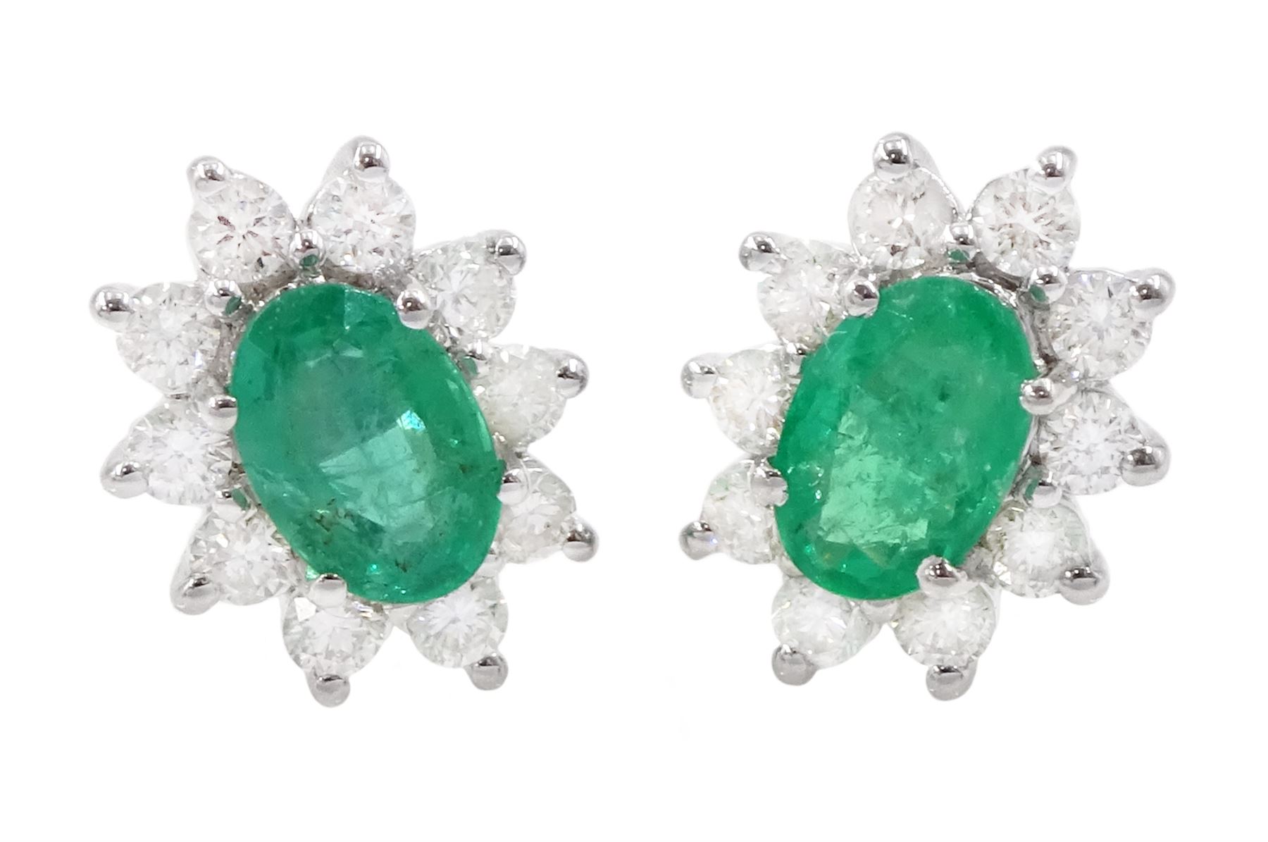 Pair of 18ct white gold emerald and diamond cluster earrings, each stud set with a single oval cut emerald surrounded by round brilliant cut diamonds, stamped, total emerald weight approx 0.90 carat, total diamond weight approx 0.60 carat