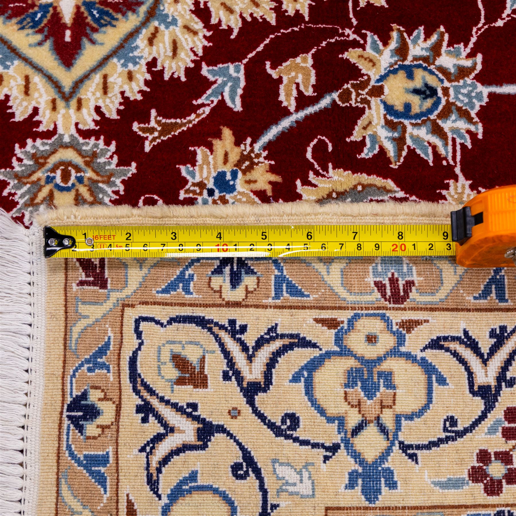 Central Persian Nain hand-knotted rug, crimson field, with central ornate ivory medallion with scrolling arabesques and flowering vine ornaments within a dense floral lattice framed by pale blue corner spandrels and enclosed with an ivory border of scrolling vine and palmette decoration between multiple guard stripes, with cotton fringe ends 