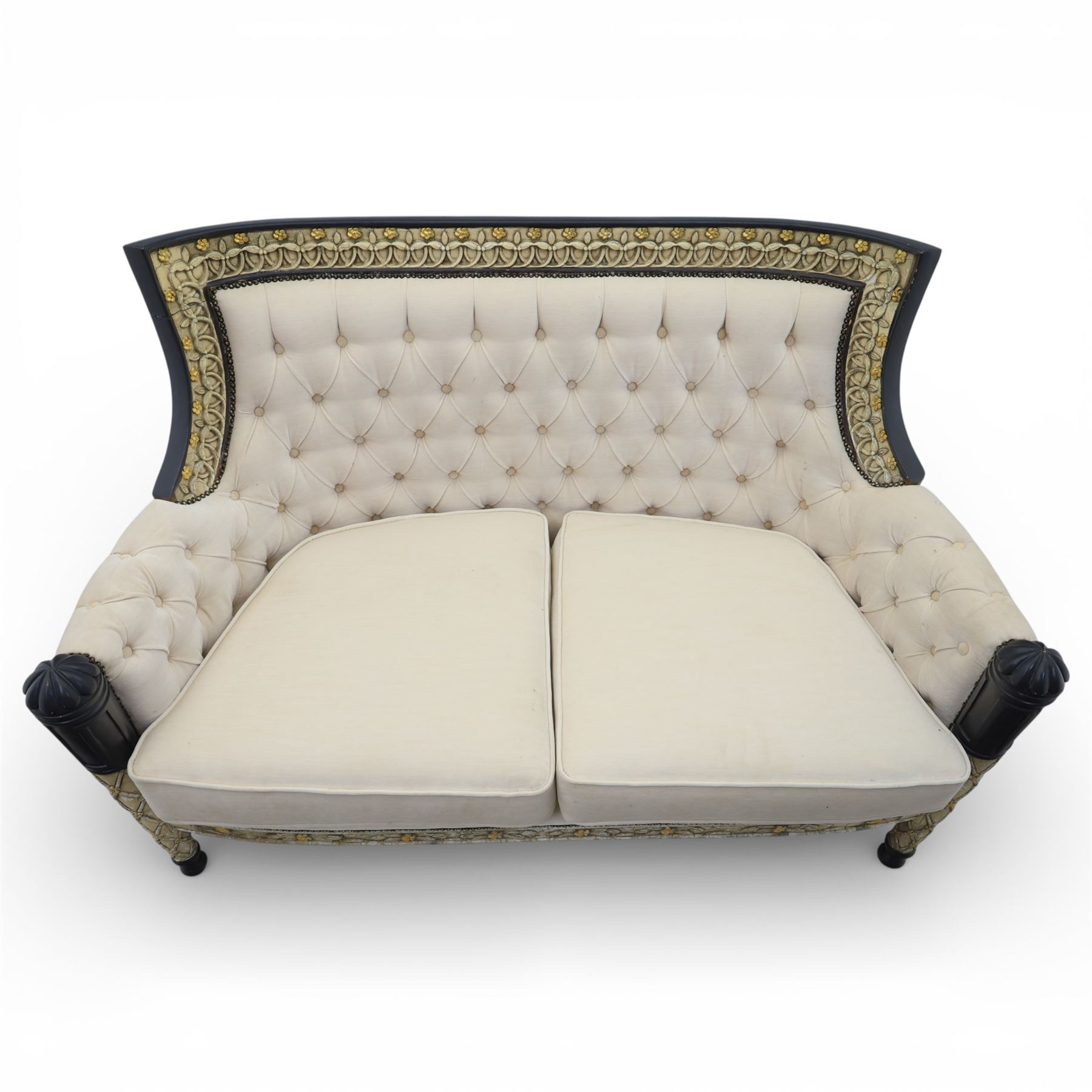 20th century Louis XVI style settee, upholstered in cream fabric with buttoned back and arms, and plain seat cushions, the shaped and black painted frame with entwined foliate detail and gilt flower heads, upon column legs with bun feet
