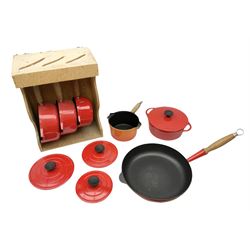 Le Creuset 'Volcanic Orange' cast iron and enamel milk pan with wood handle together with a three piece red cast iron Cousances saucepan set of graduating form, with lids housed in original wooden hanging stand and further Cousances lidded casserole dish and pan