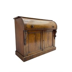 Victorian mahogany roll-top writing desk, top concealing fitted interior with pigeonholes and three drawers, the trisector inset writing surface with writing slope, base fitted with panelled cupboard enclosing single shelf, decorated with scrolled corbels