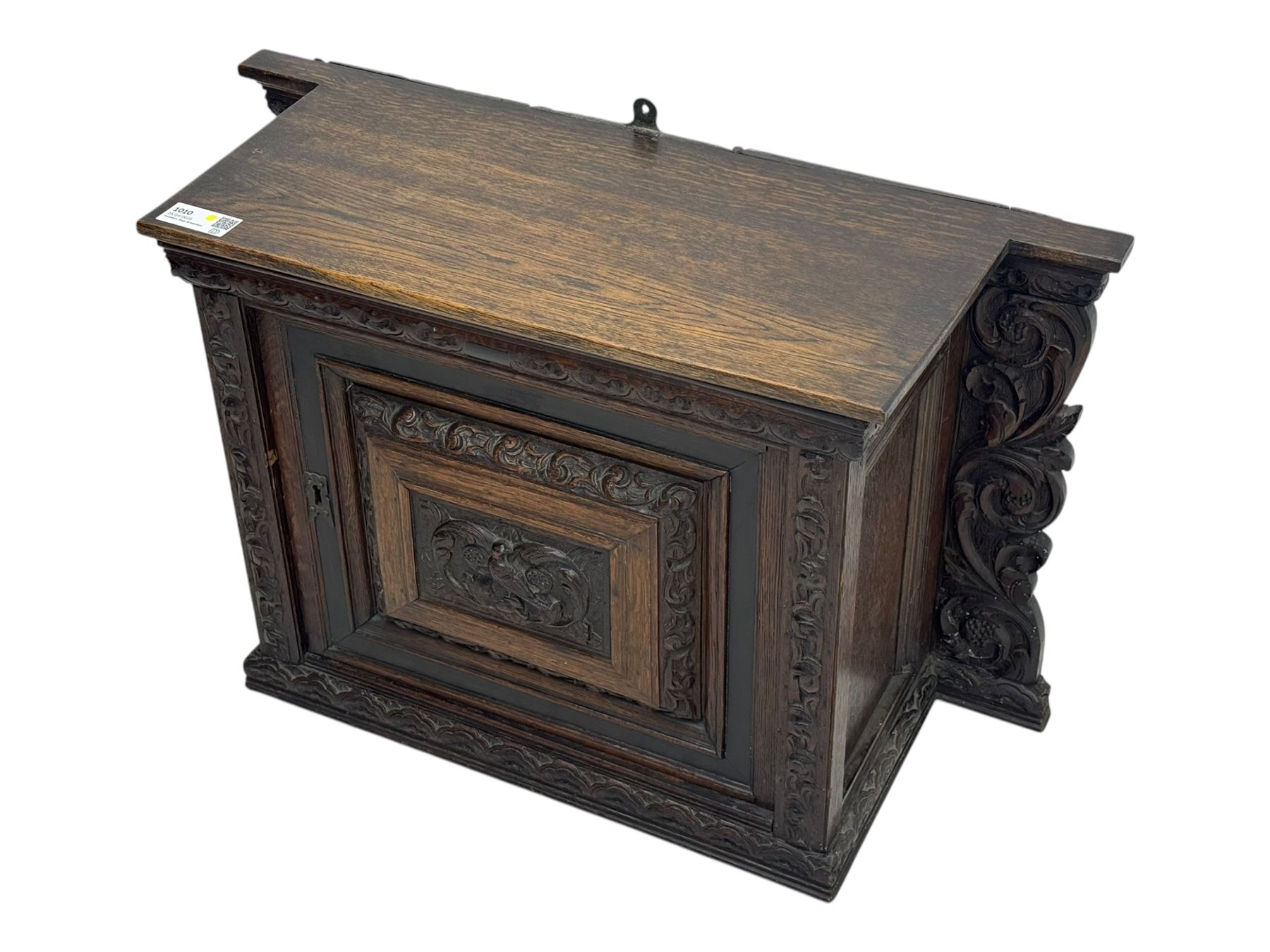 18th century and later carved oak cupboard, enclosed by panelled door carved with central bird motif and scrolled leafage with an outer ebony band, the frieze and uprights carved with repeating lunette and floral designs, flanked by scrolled foliate carved upright brackets