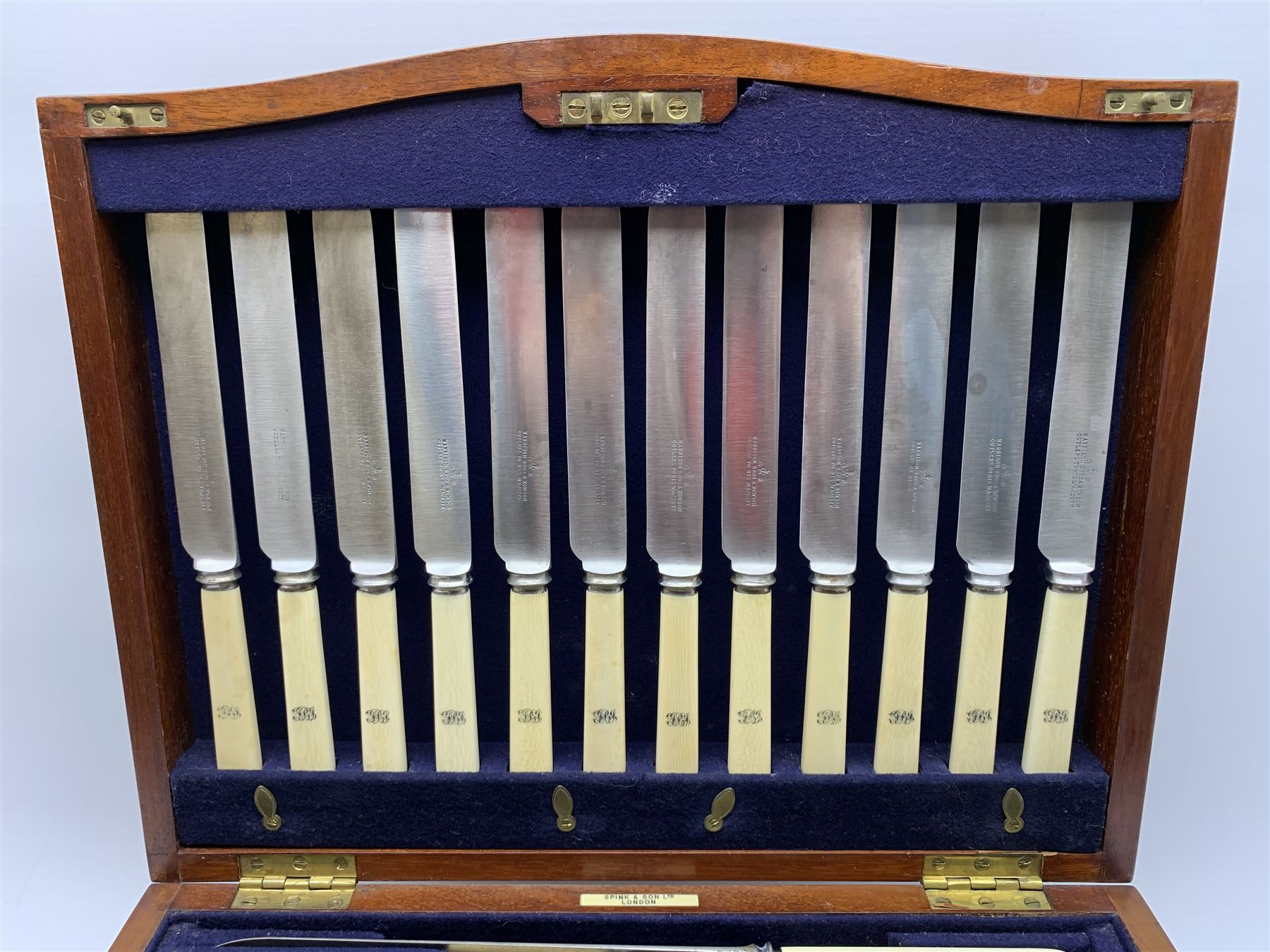 Late 19th/early 20th century composite canteen of silver flatware, contained within an early 20th century mahogany serpentine fronted case with twin drop carry handles, and hinged cover with boxwood stringing and central inlaid shell motif, above a single drawer with twin ring handles and Wellington style locking system, the cover and drawer opening to reveal plaque for Spink & Sons Ltd London, and fitted interior containing ivory handled knives, ivory handled carving set, and silver Hanoverian and Old English pattern cutlery, each with engraved monogram to terminal, hallmarked London, makers Spink & Son (John Marshall Spink), Goldsmiths & Silversmiths Co, and Chawner & Co (George William Adams), various dates ranging 1880-1923, gross weighable silver 92.59 ozt (2880 grams)