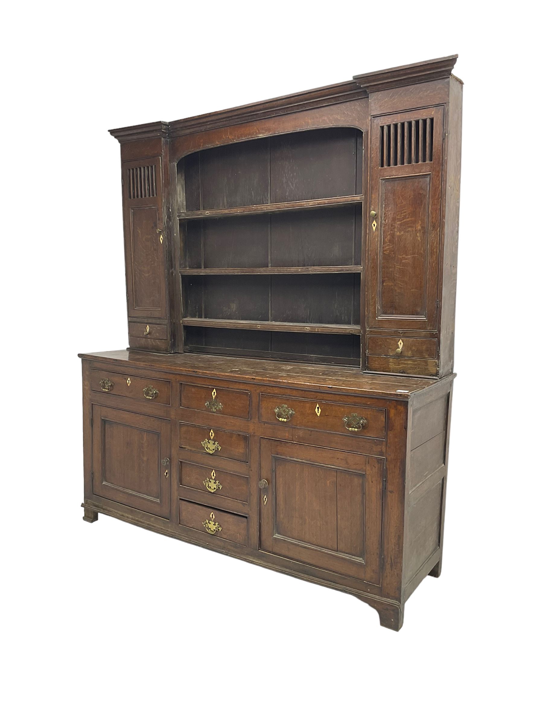 George III oak dresser, projecting cornice over three tier plate rack flanked by reeded uprights and two cupboards, enclosed by slatted and panelled doors above small drawers, the lower section fitted with six drawers and two cupboards, on bracket feet