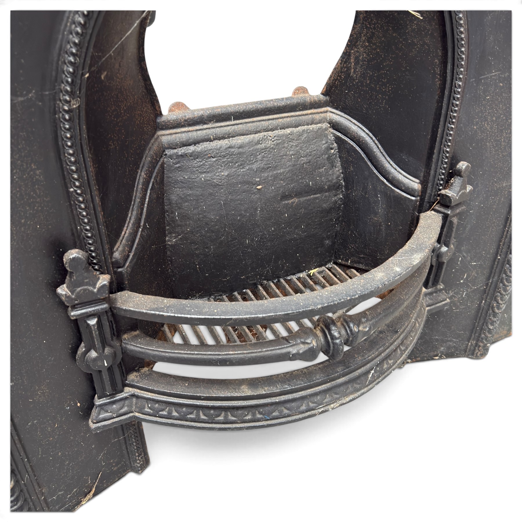 Late Victorian black-painted cast iron fireplace, the arched surround with anthemion cartouche and guilloche-moulded border, enclosing a bow-front fire basket with finialled standards, railed front and leaf-cast apron, with sheet-metal backplate