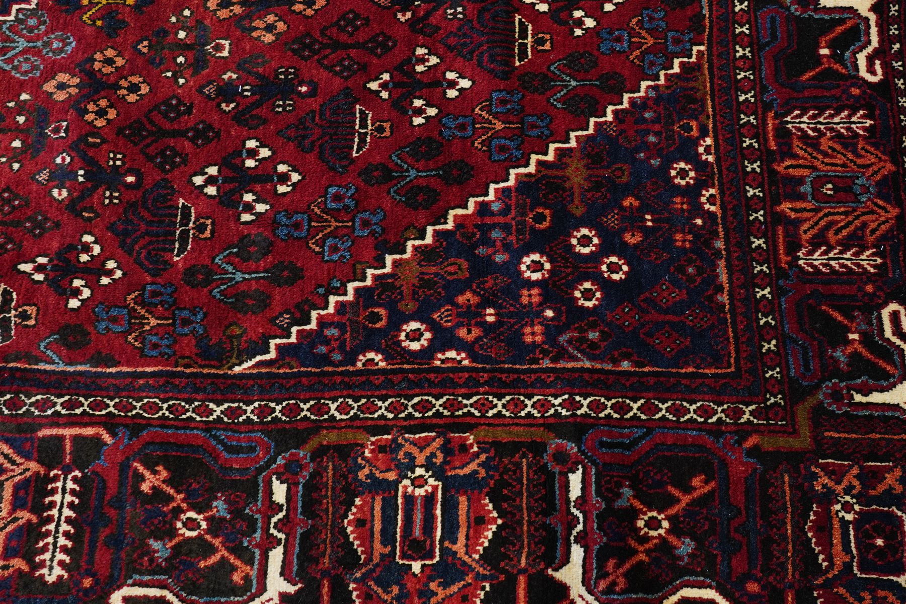 Central Persian Joshaghan hand-knotted carpet, deep red field decorated with a lattice design of stylized boteh and palmette motifs arranged around a stepped diamond medallion, navy corner spandrels similarly decorated enclosed by a dark indigo main border of floral and geometric motifs between multiple guard stripes, with cotton fringe ends 