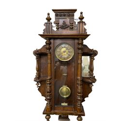 An imposing early 20th century German mahogany cased wall clock c1910, within a shaped surround with turned columns incorporating two mirror backed shelves (one mirror missing) with a carved pediment and matching finials, full length arched door with integral turned columns, 7' two-piece dial with a pressed gilt centre, roman numerals, minute markers and pierced steel gothic hands, gridiron pendulum with a pressed brass bob and beat plate, eight-day spring driven movement striking the hours and half hours on a coiled gong.  

