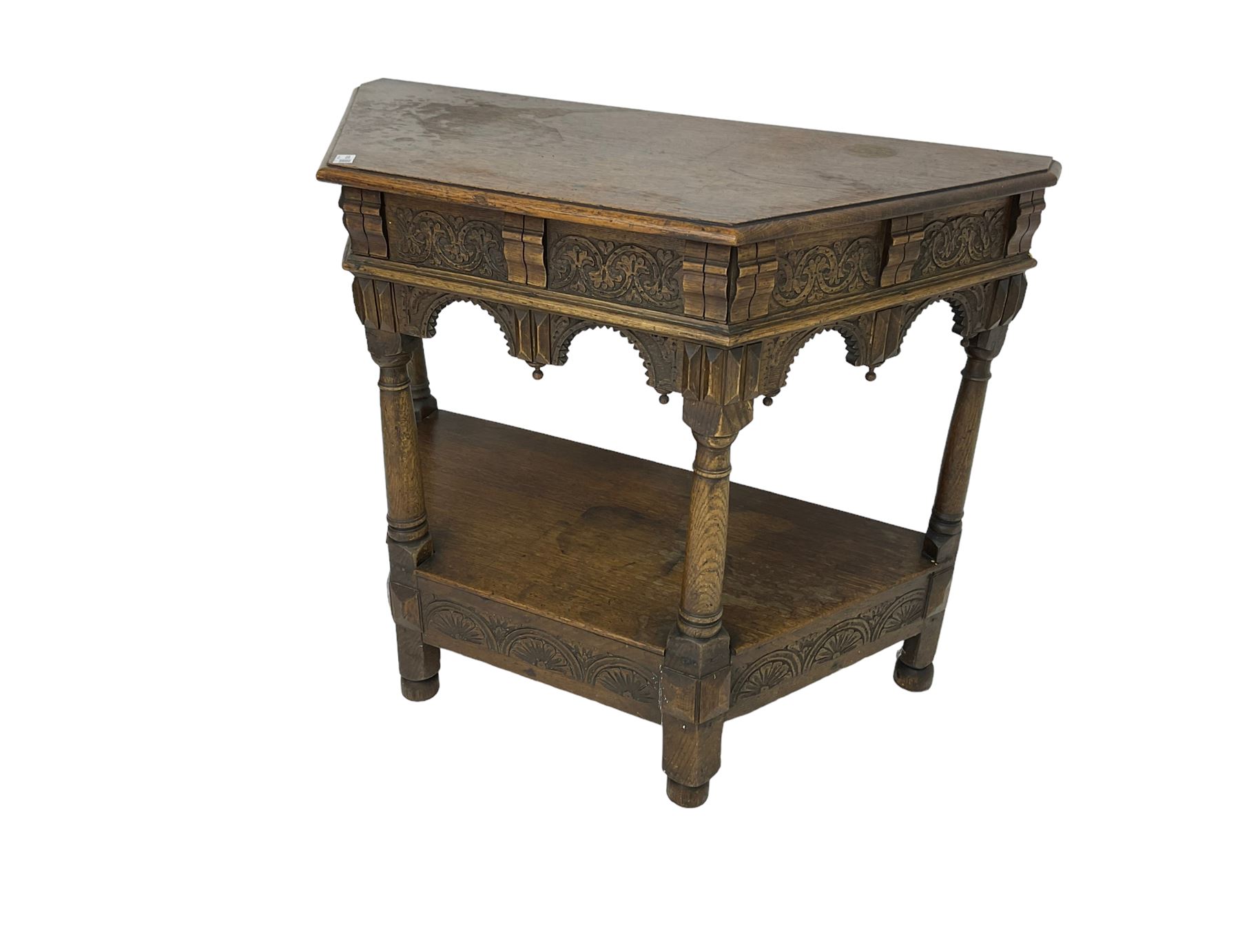 Jacobean design carved oak side or credence table, demi-heptagon top with moulded edge, frieze carved with foliate C-scroll design above ornate arcade carved apron, under-tier united by ring turned pilisters, lower frieze carved with repeating lunettes