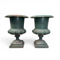 Pair of Victorian cast iron campana garden urns, the flared rim with repeating stylised anthemion motifs with scrollwork, over a deep gadrooned and Aesthetic moulded underbelly, fluted and foliate lower bowls on square pedestal bases, in antique green-painted finish
