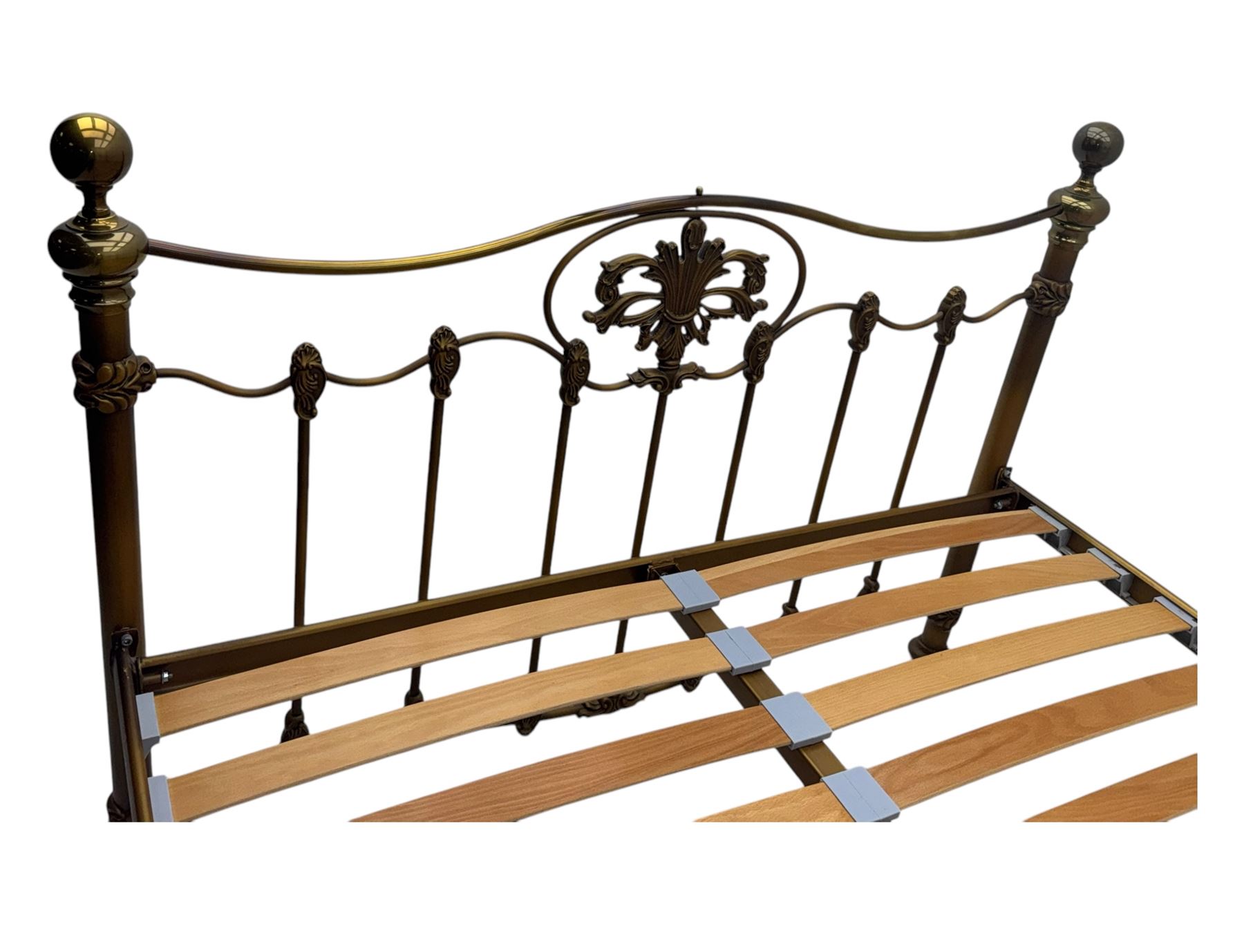 Victorian design king size brass bed frame, featuring an arched headboard and footboard with intricate cast floral and scrollwork centre motifs, flanked by cylindrical supports with ball finials and decorative collars, raised on rounded feet, with a slatted wooden base