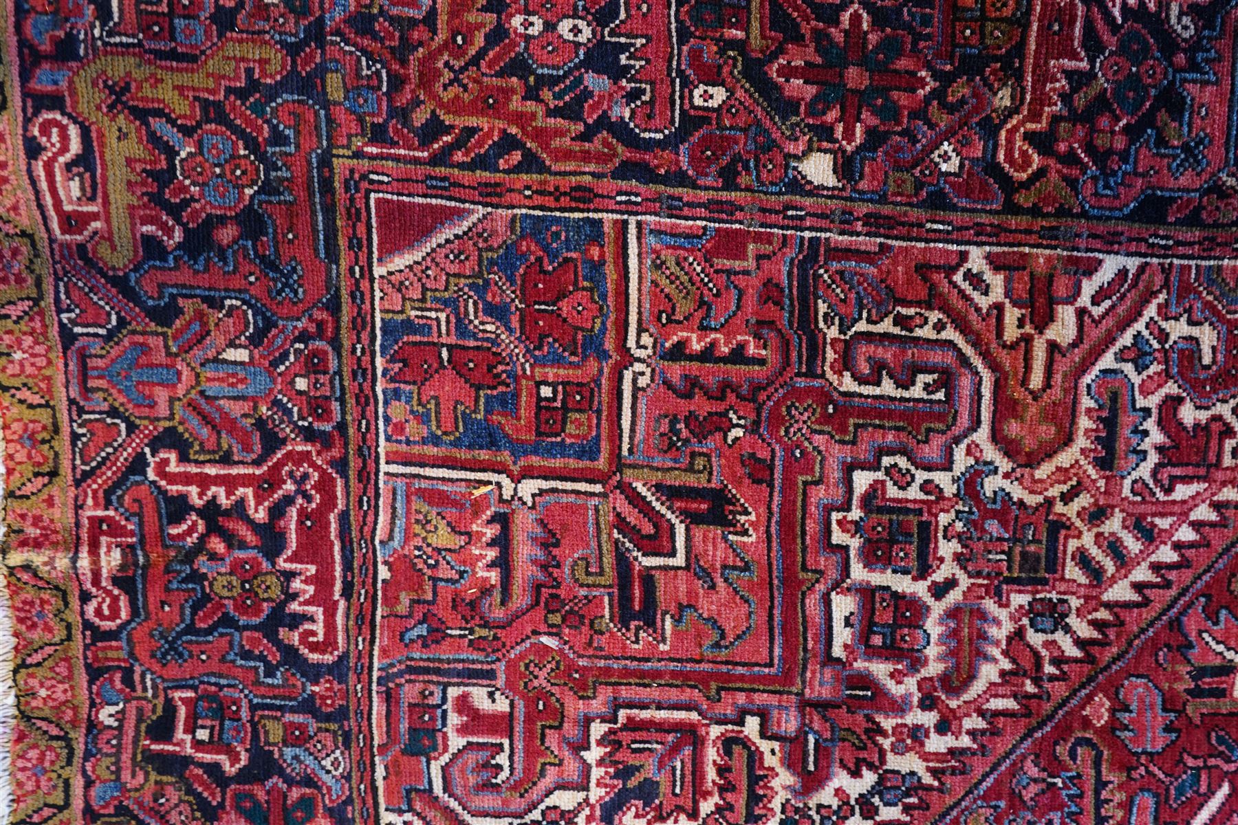 North West Persian Heriz hand-knotted carpet, brick-red field with a large central angular star medallion with pendant motifs, surrounded by stylized geometric palmettes, serrated leaves and tribal devices, ivory corner spandrels similarly decorated, field enclosed by a dark indigo main border of stylized rosettes and angular vine motifs between multiple guard stripes, with cotton fringe ends  