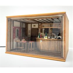 Dolls house scale room setting of a public house bar with tiled floor and beam and plaster ceiling and walls, bench seat, stools and table set out with a meal and drinks, large planked finish canted bar well stocked with food, drinks, bottles, glasses etc and bartender figure behind; electrically illuminated with sliding perspex access panel to front W38cm D28cm H24cm