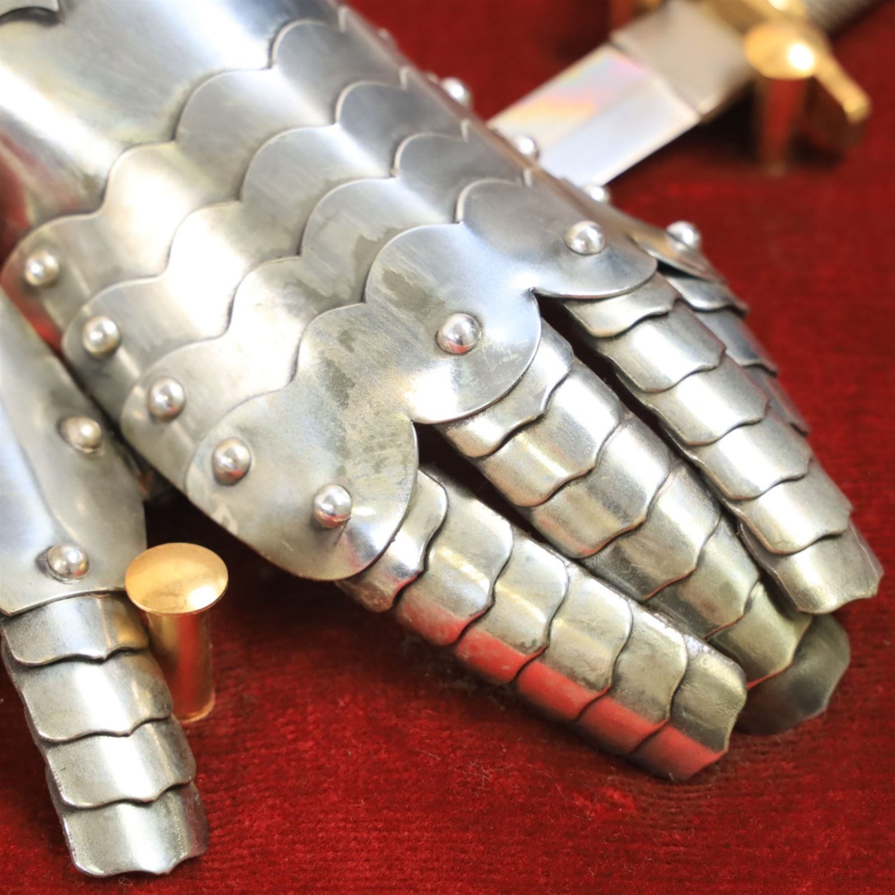 Three replica gauntlets, each housed upon a red wall shield, two with daggers, the third with a sword, largest H102cm