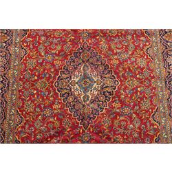 Persian Kashan hand-knotted carpet, madder red ground centred by shaped dark navy, ivory and pale blue floral medallion with pendants, surrounded by scrolling vines, palmettes and flowerheads, dark navy spandrels, enclosed by dark navy floral border with multiple floral guard stripes