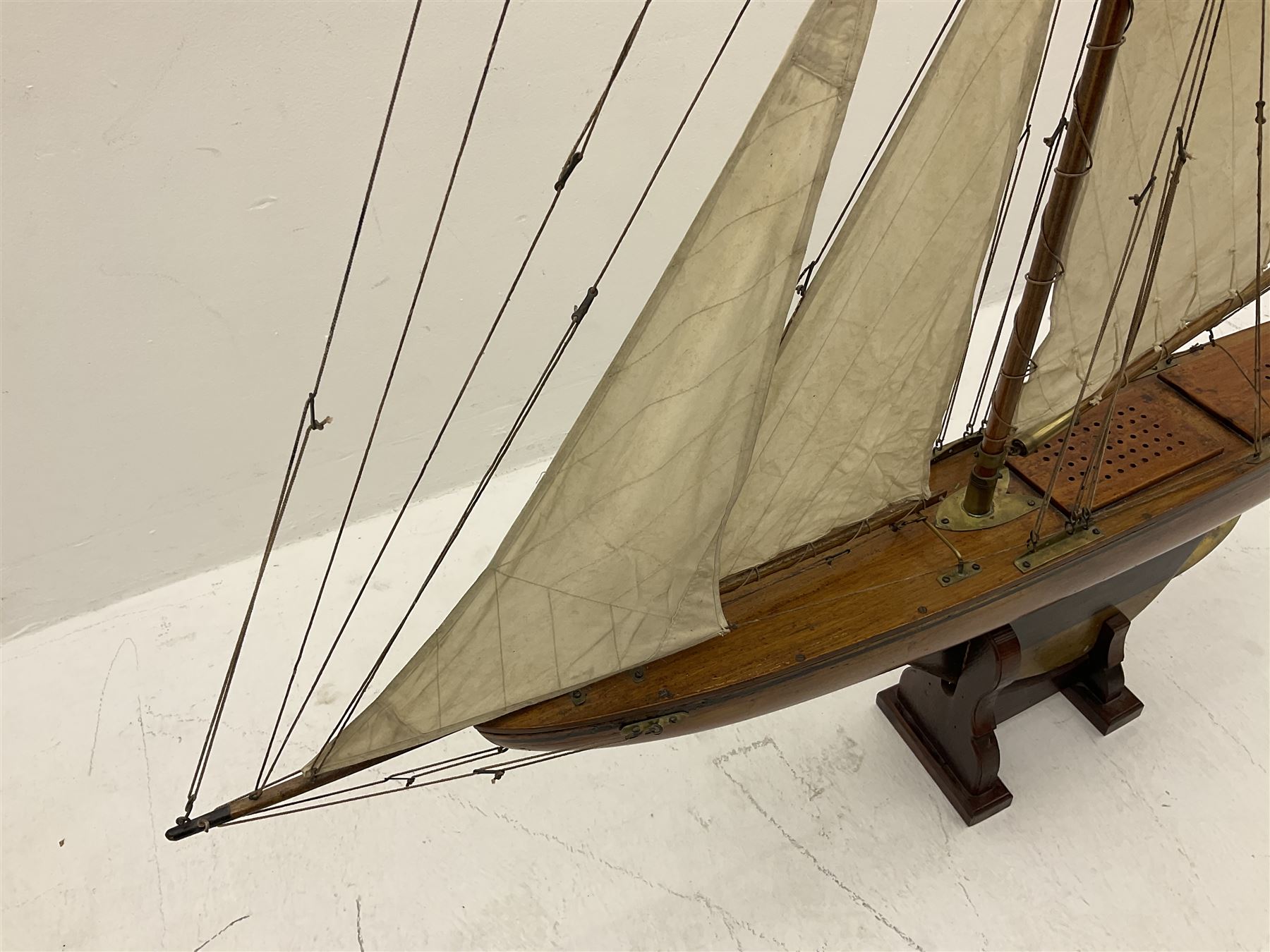 Early 20th century large pond yacht with mahogany hull, stained pine keel with brass rudder, simulated deck hatches and brass fittings, rigged as a staysail schooner (?) with four sails L117cm H148cm; loose mounted on stained pine stand