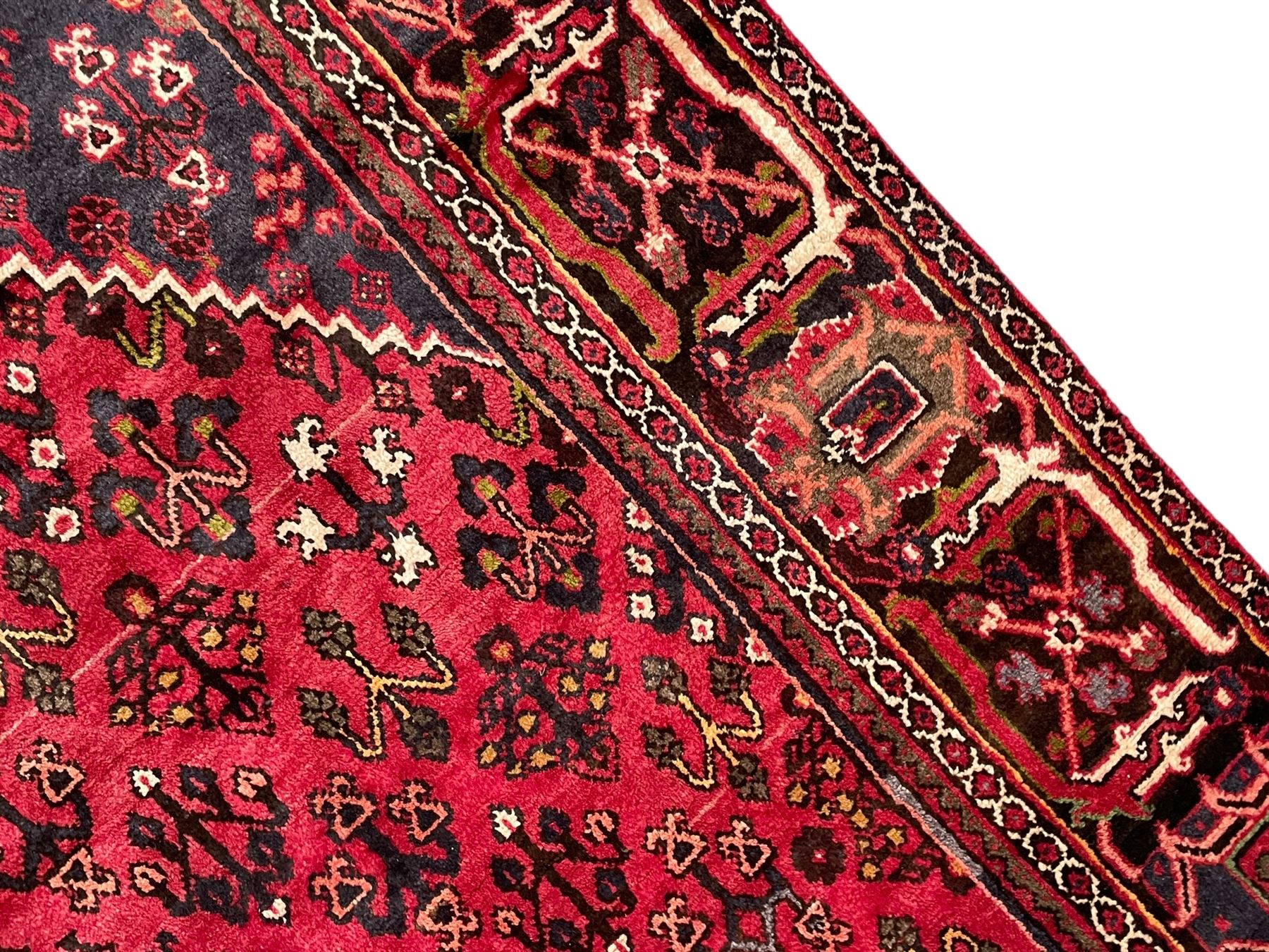 Persian Joshaghan crimson ground rug, stepped lozenge medallion surrounded by repeating foliate lozenge motifs, the border decorated with stylised plant motifs, within geometric guard stripes 
