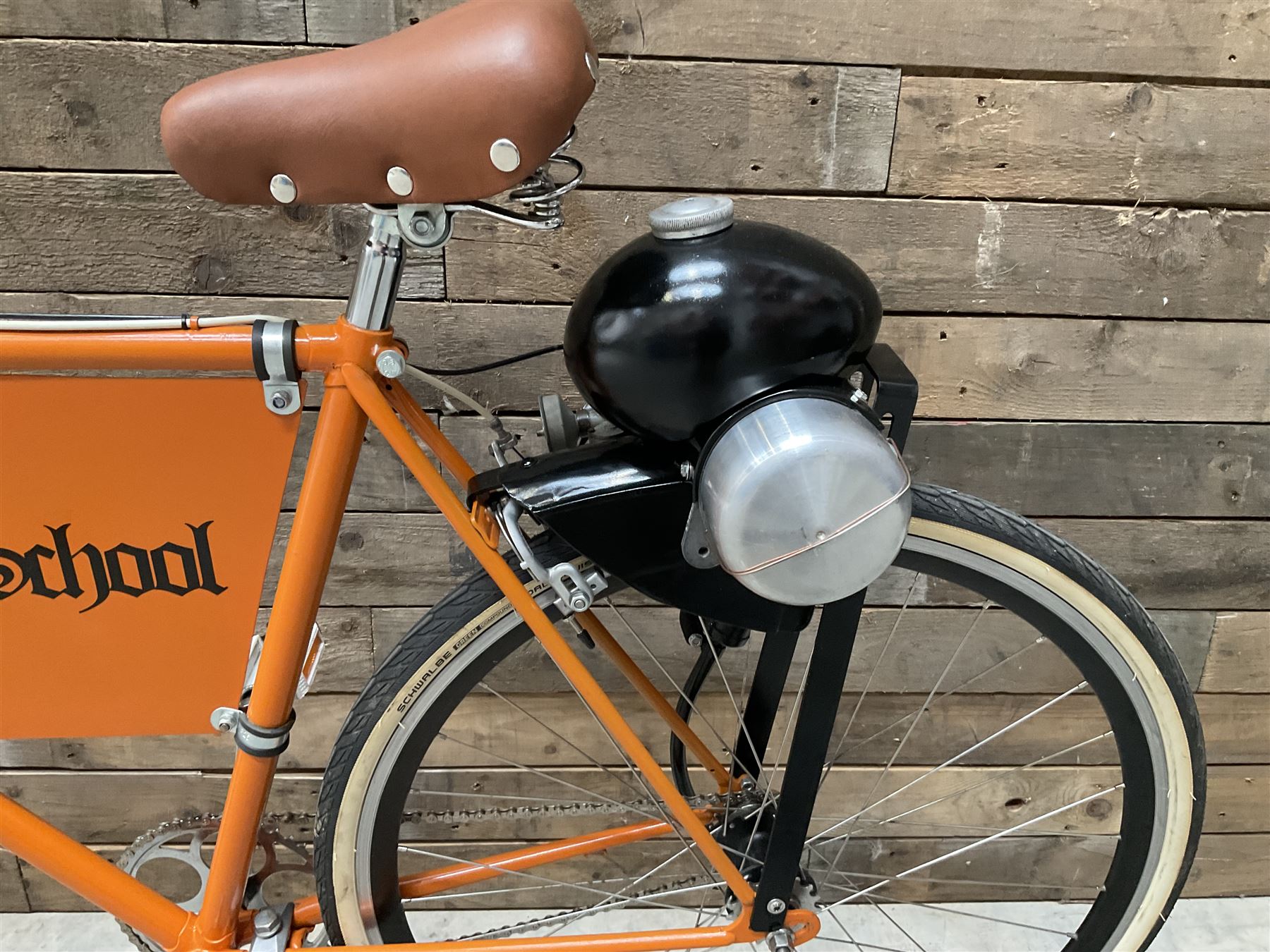 Fully restored vintage advertising bicycle with 2 stroke petrol engine, orange frame, tan leather seat