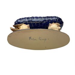 Ceramic 'girl and boy dish', by Helen Kemp, an oval dish with a mottled pink ground and gilt edging upon the sculpted heads of a girl and a boy, together with a 'boy sconce', by Helen Kemp, a sculpted boy holding a small bowl with foliate decoration, both with the artist's mark beneath.