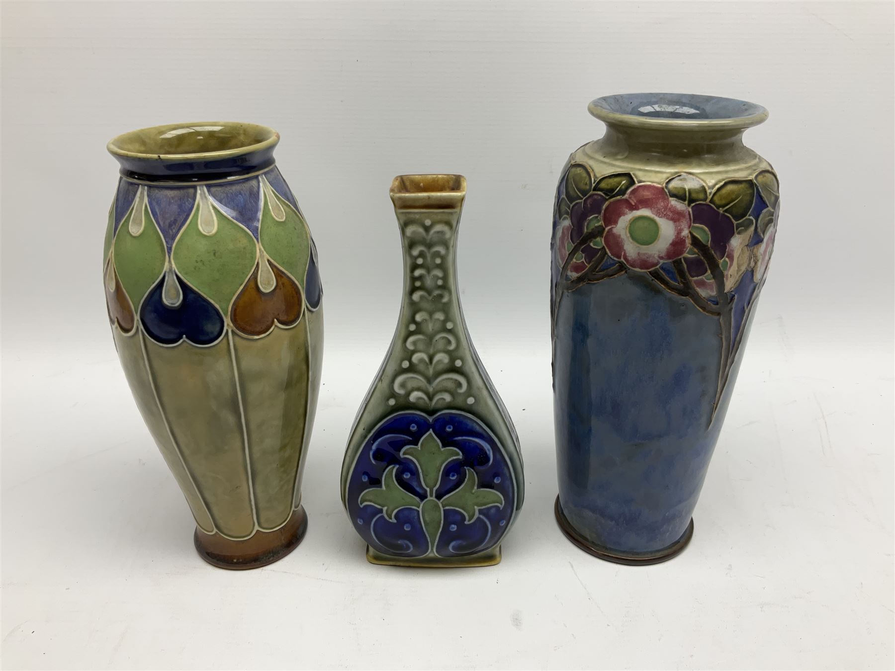 Two Royal Doulton stoneware vases, the first example with tubelined floral decoration, the second with Art Nouveau decoration, together Doulton Lambeth vase of flattened form with foliate decoration on a green ground, all with impressed mark beneath, tallest example H26cm