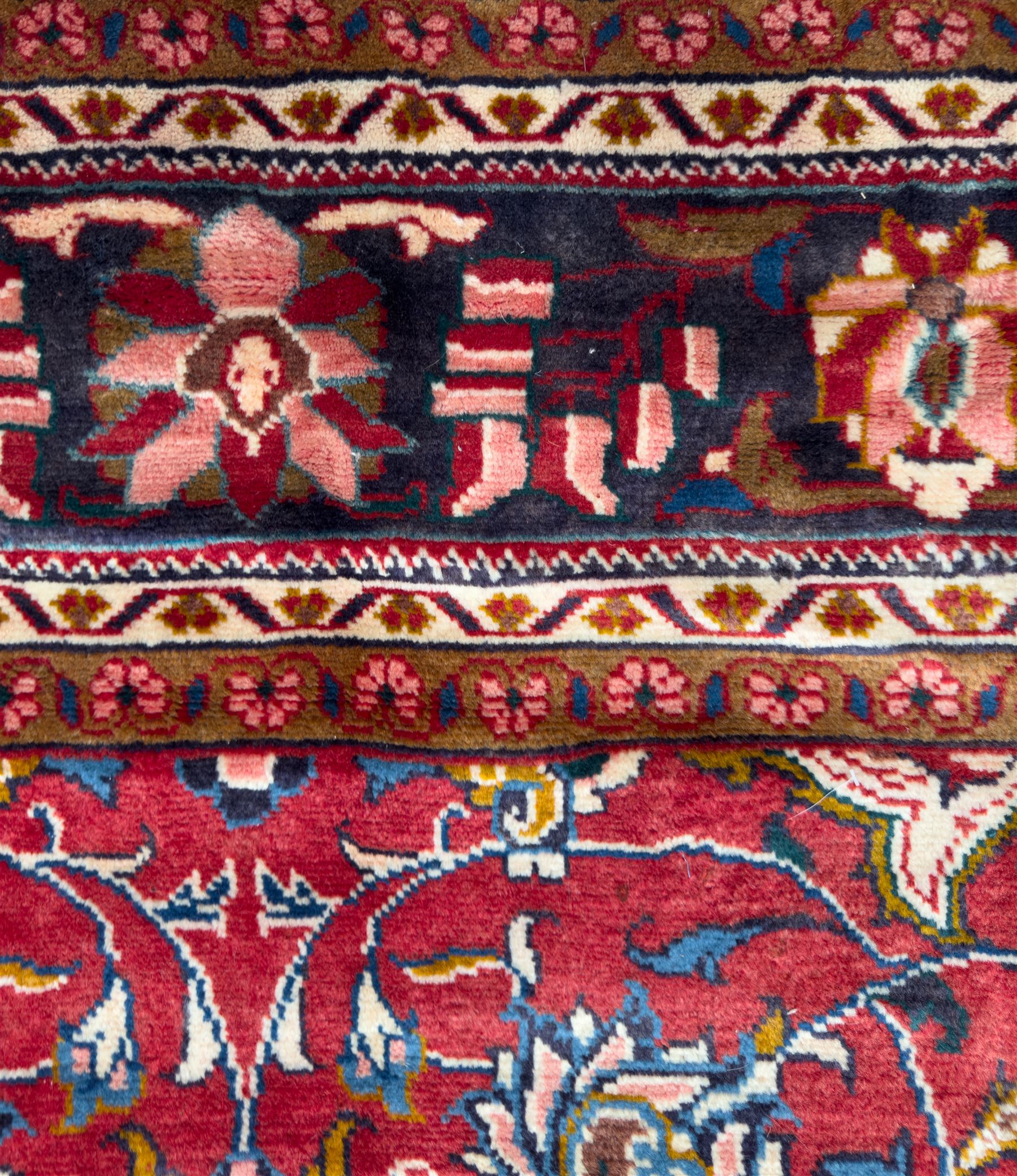 Northwestern Persian Lillihan hand-knotted carpet, madder red field with scrolling vines, rosettes, and palmettes around a central circular medallion in navy, ivory and ochre, and ivory ground spandrels within a navy border of stylized flowerheads and vines between multiple guard stripes 