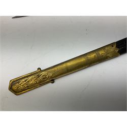 WW1 George V era 1827 Pattern Royal Naval Officer’s sword, the 80cm fullered steel blade decorated with crown, fouled anchor etc and marked Gieves Portsmouth London Edinburgh Devonport to the ricasso, gilded hilt with fouled anchor and crown, wire-bound ray skin grip, lion’s head pommel with mane backstrap, folding/locking langet and full bullion knot; in  leather scabbard having twin brass lockets with hand engraved panels and twin suspension rings L94cm overall. Provenance: By direct family descent from Brian Heathcote HMS Conqueror later Superintendant in the Liverpool Special Constabulary.